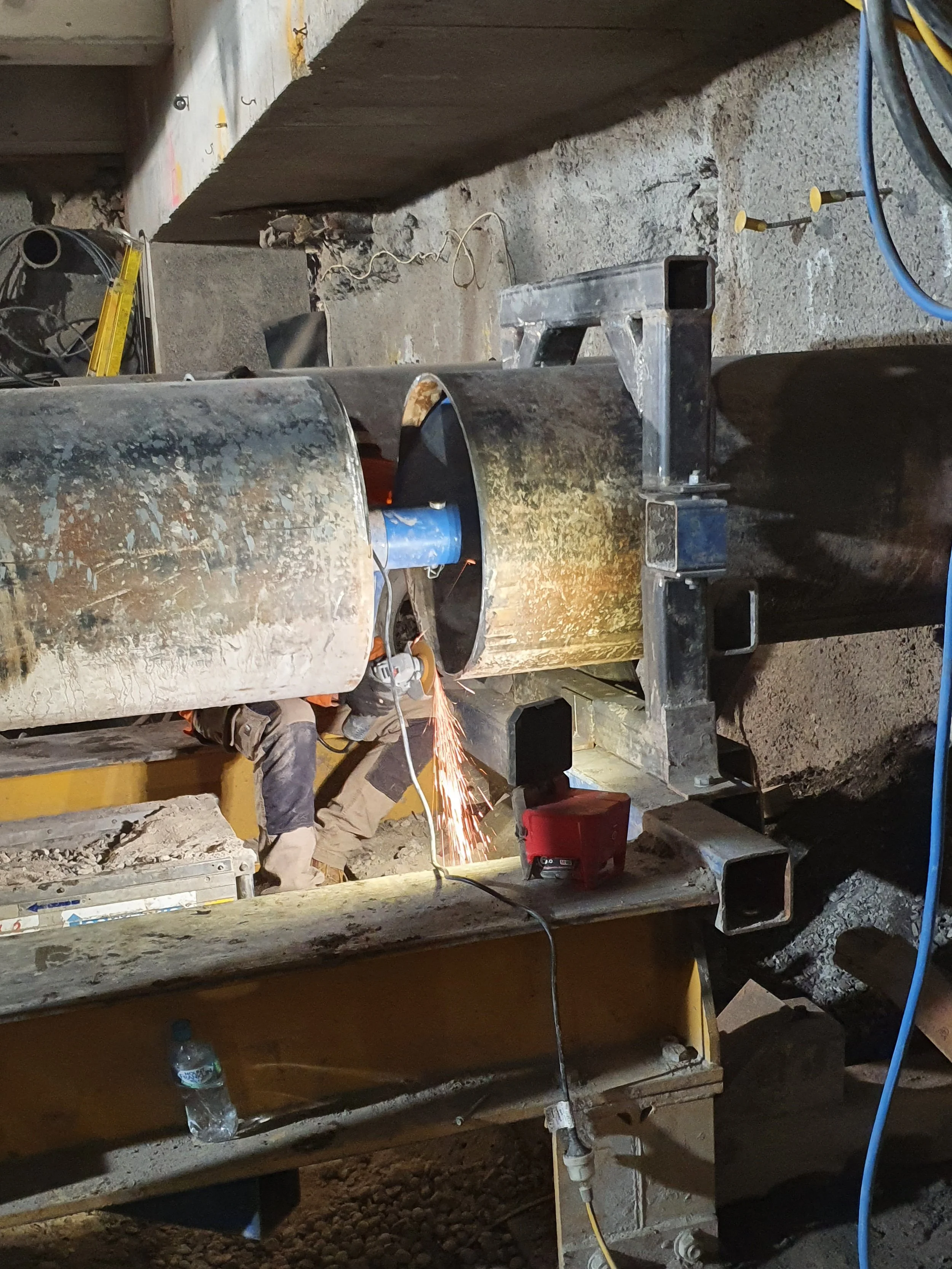 Construction worker welding a large metal pipe in an industrial or construction setting.