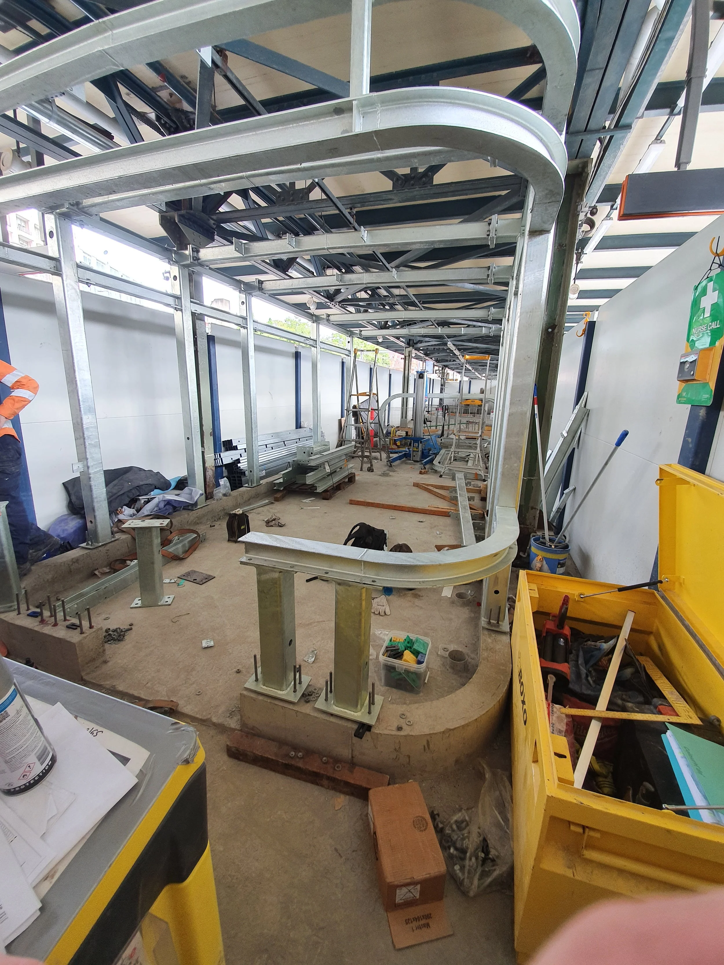Under construction interior with metal framework, construction tools, and equipment, including benches, ladders, and a yellow toolbox.