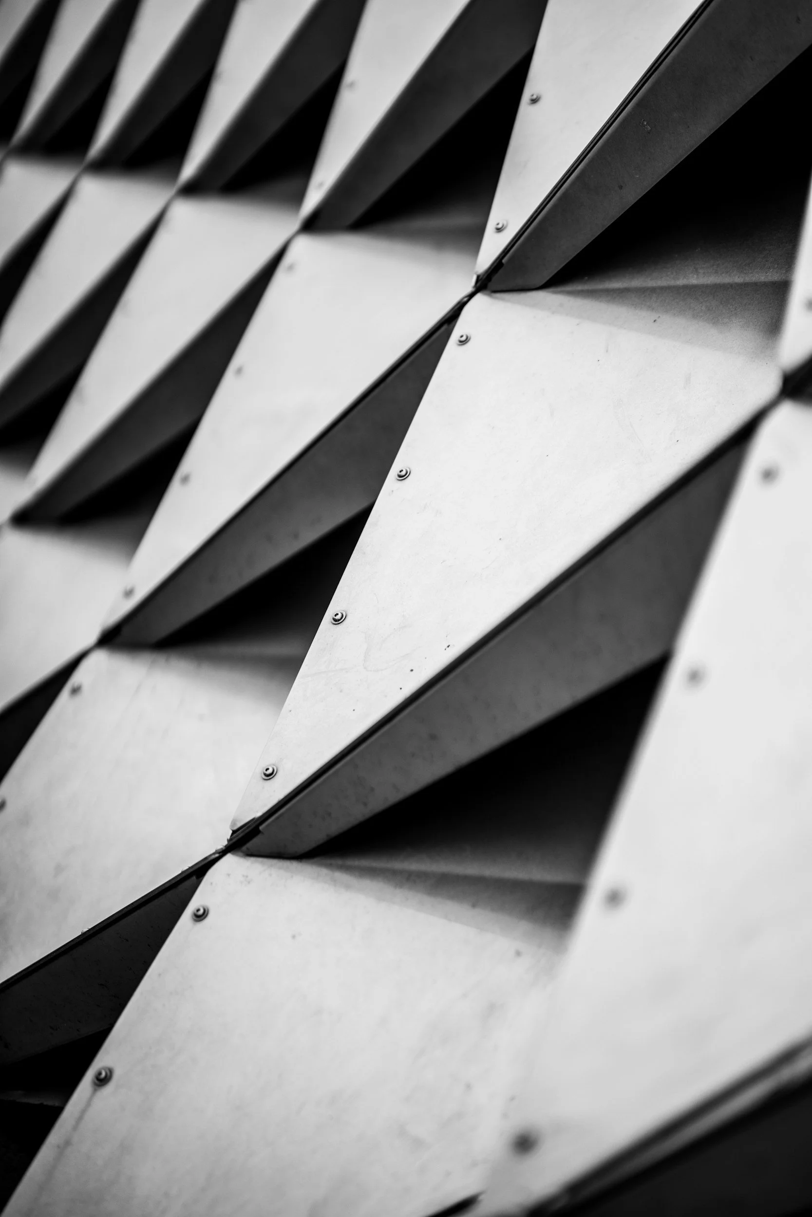 Close-up of a building facade with geometric metal panels arranged in a diagonal pattern, black and white photo.