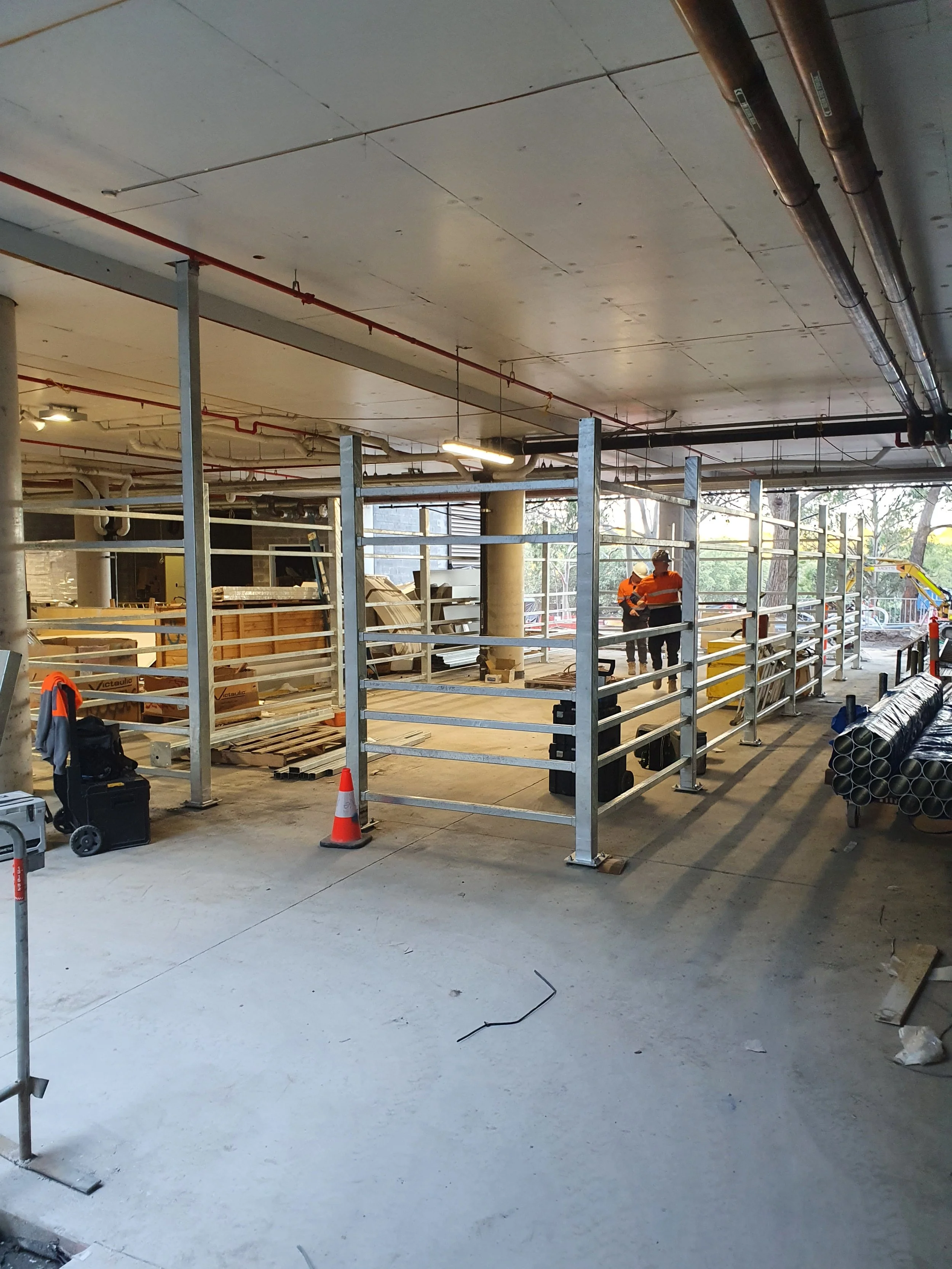 Construction site with workers in orange vests and hard hats, metal framing, pipes, and building materials.