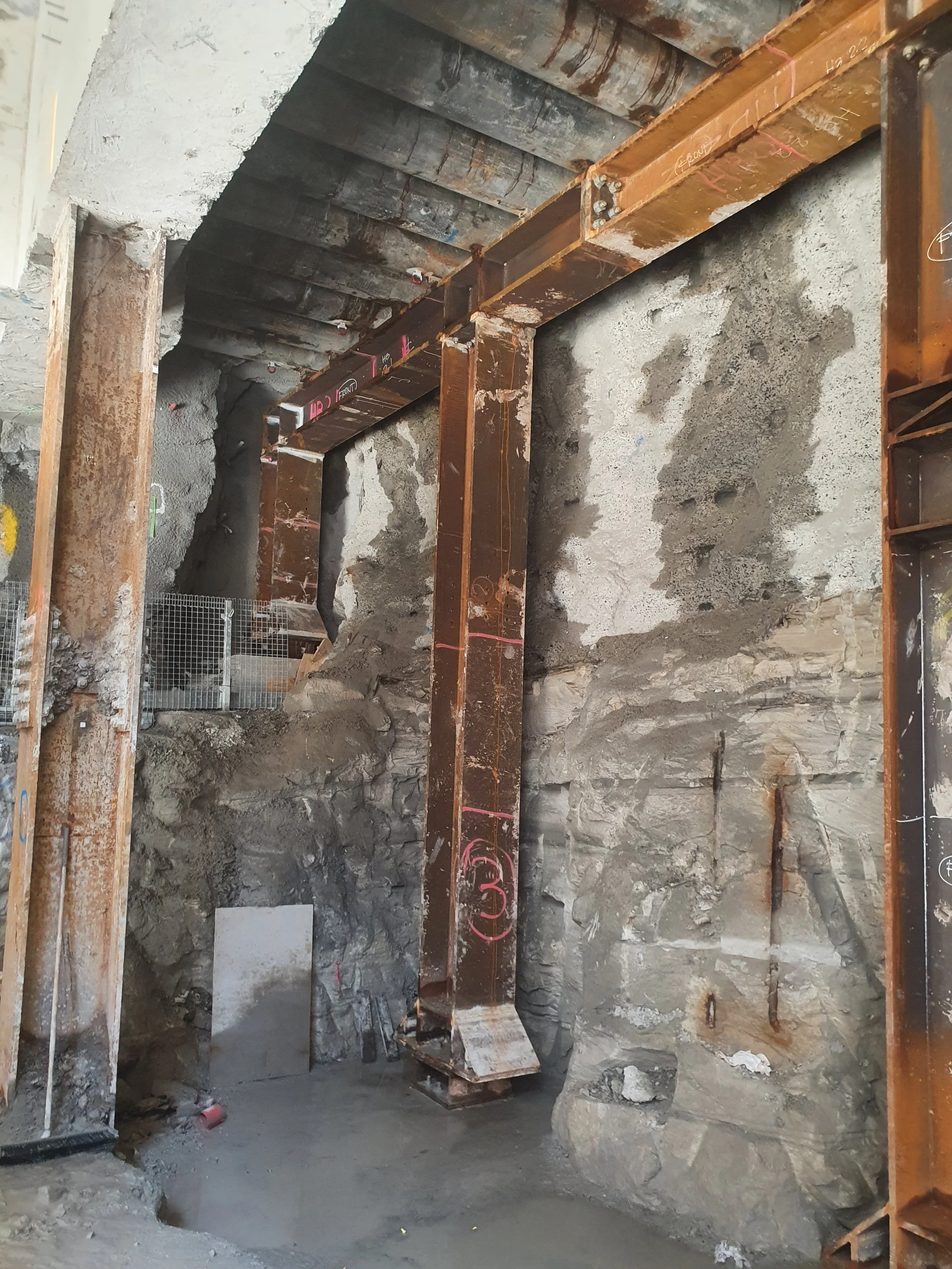 Construction site with steel beams and rocky excavation wall.