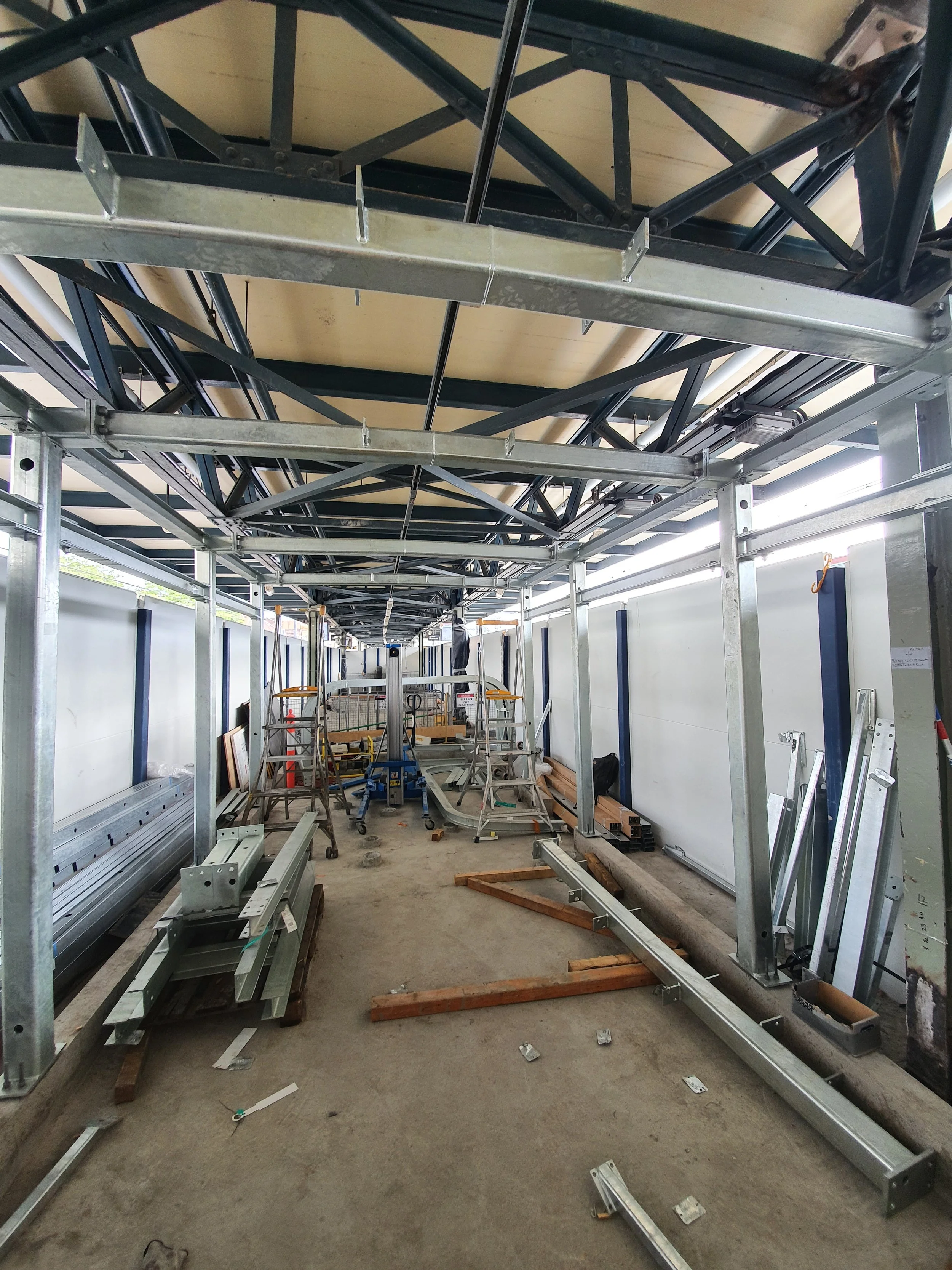 Construction site with metal framing and scaffolding inside a building, with ladders, tools, and building materials.
