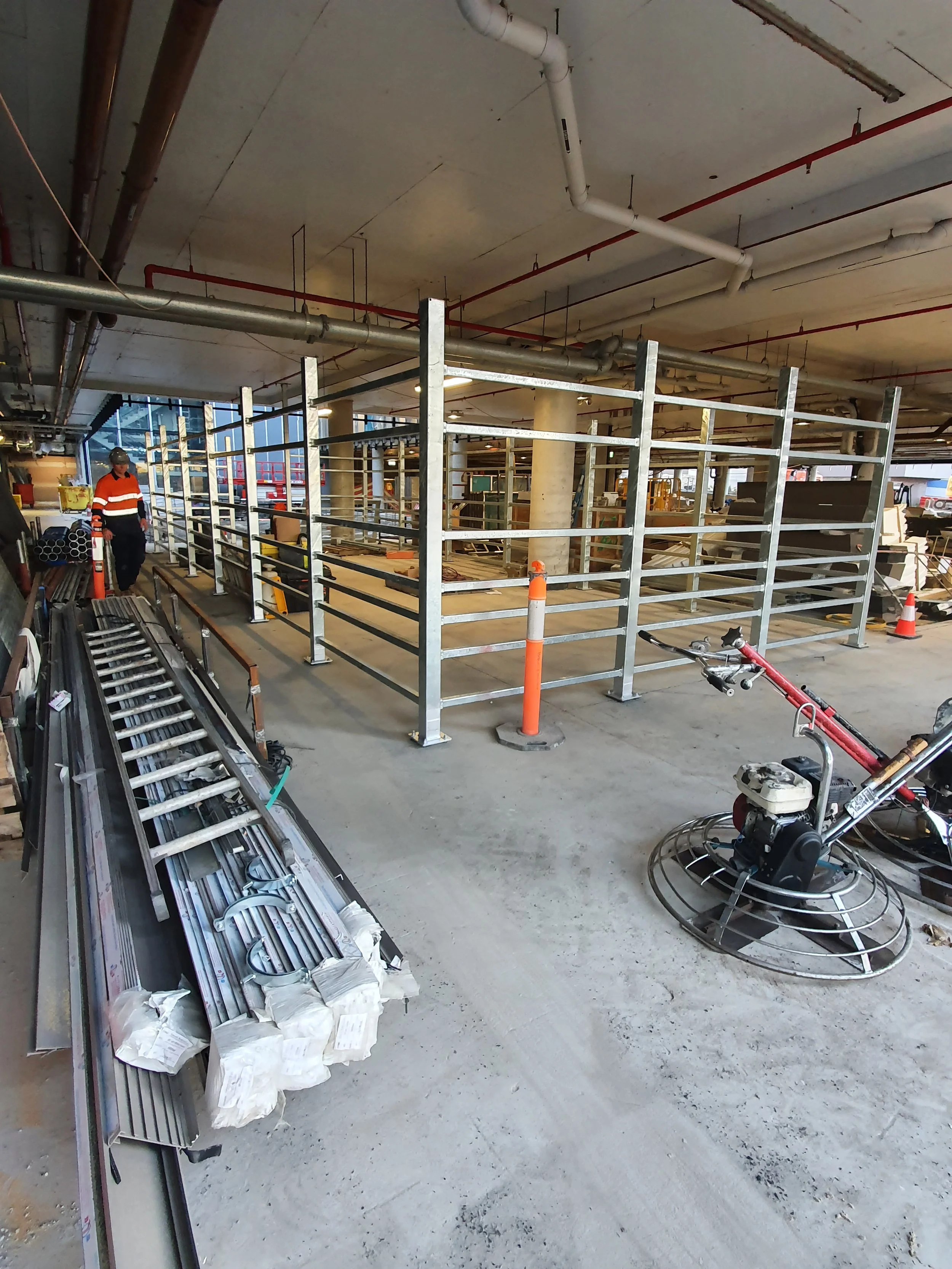 Construction site with metal railings, construction worker in safety gear, and construction tools and materials, including metal pipes and a power trowel.