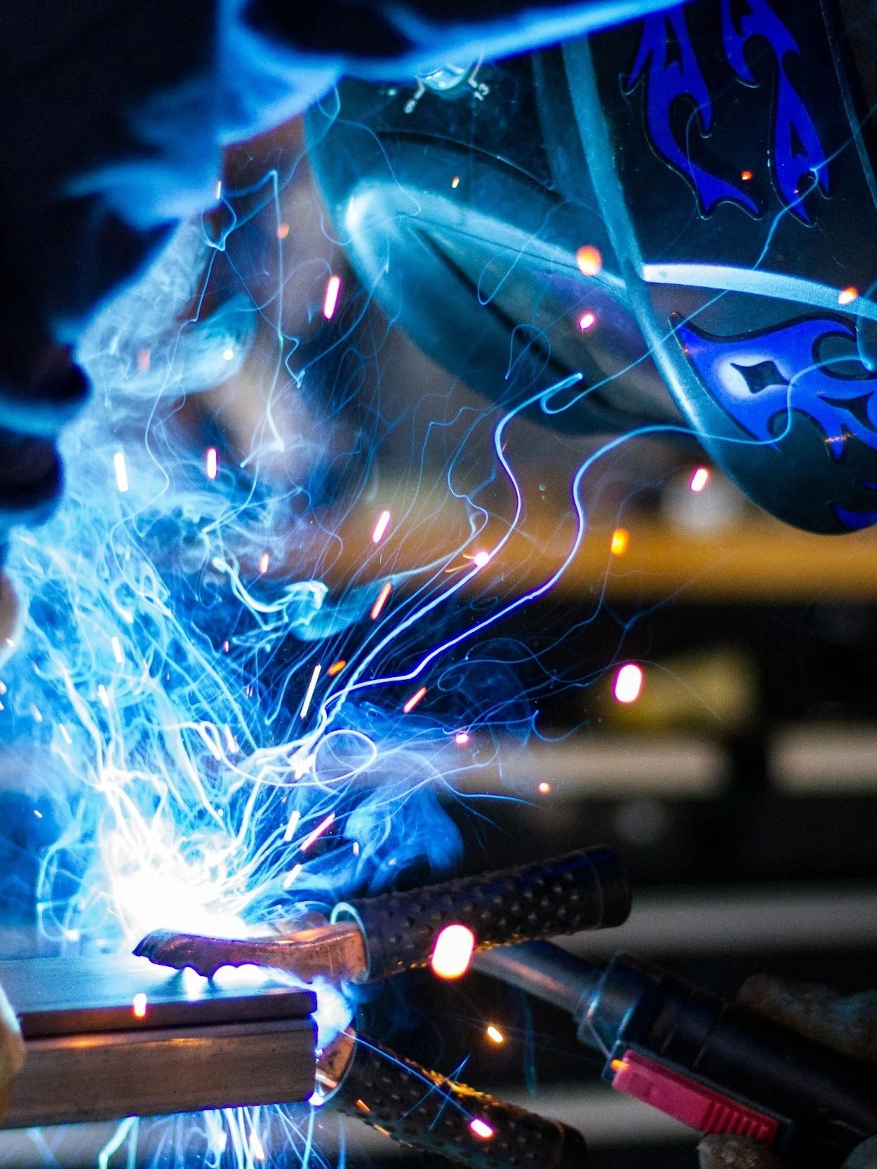 Close-up of a welding process with bright sparks and blue light, showing a welding torch and gloves.