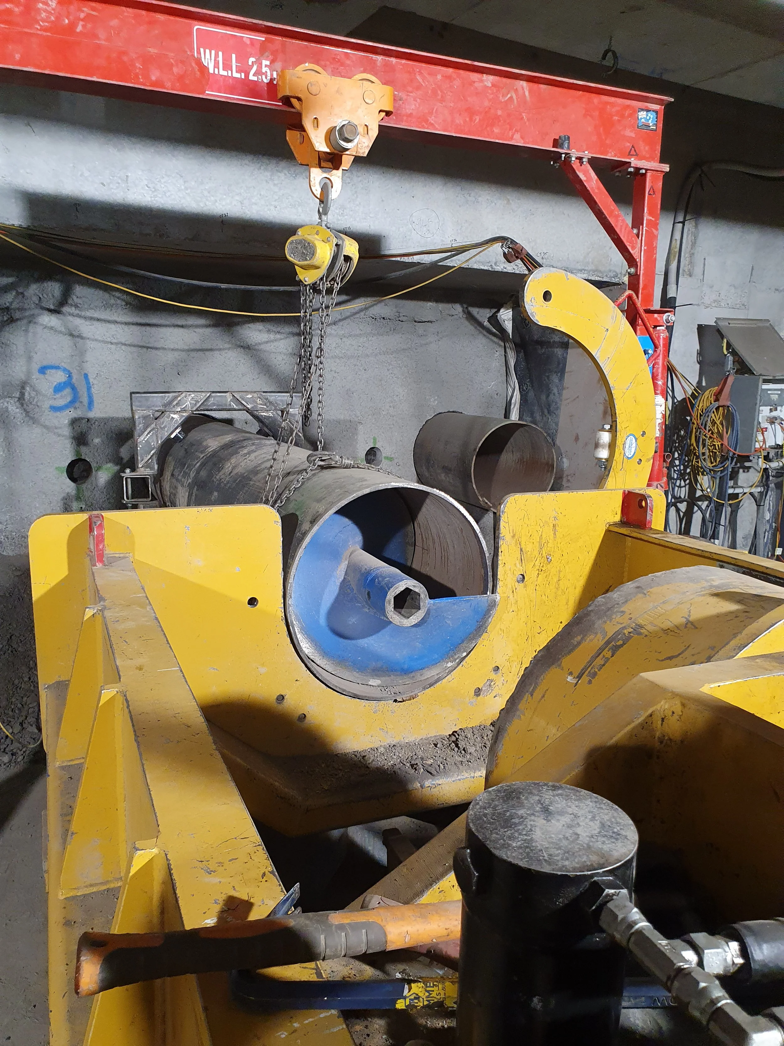 Industrial pipe welding setup with a yellow pipe clamp and a pipe in a workshop, with a crane overhead.