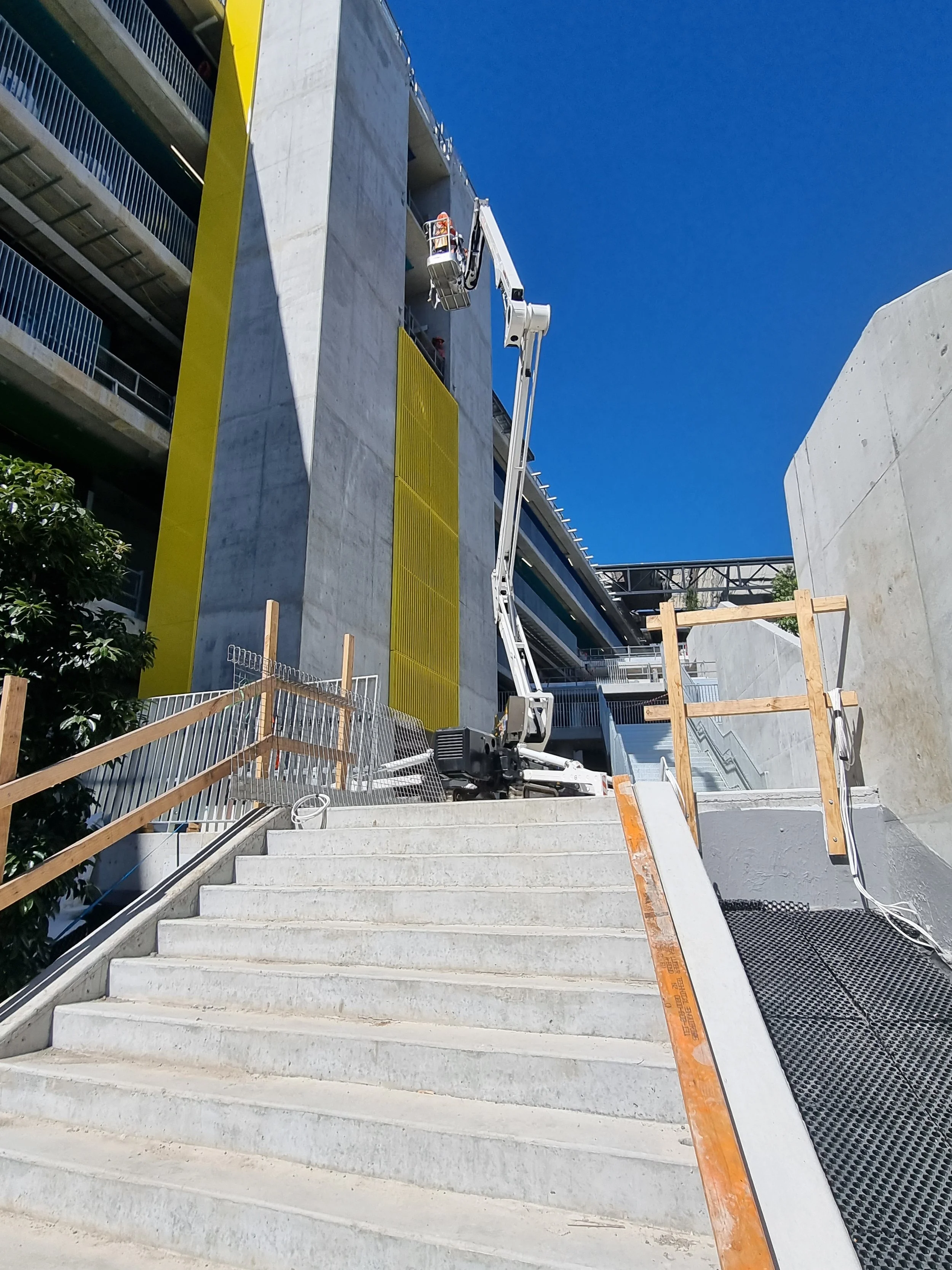 Construction site on a staircase outside a concrete building with a crane lift and safety railings.