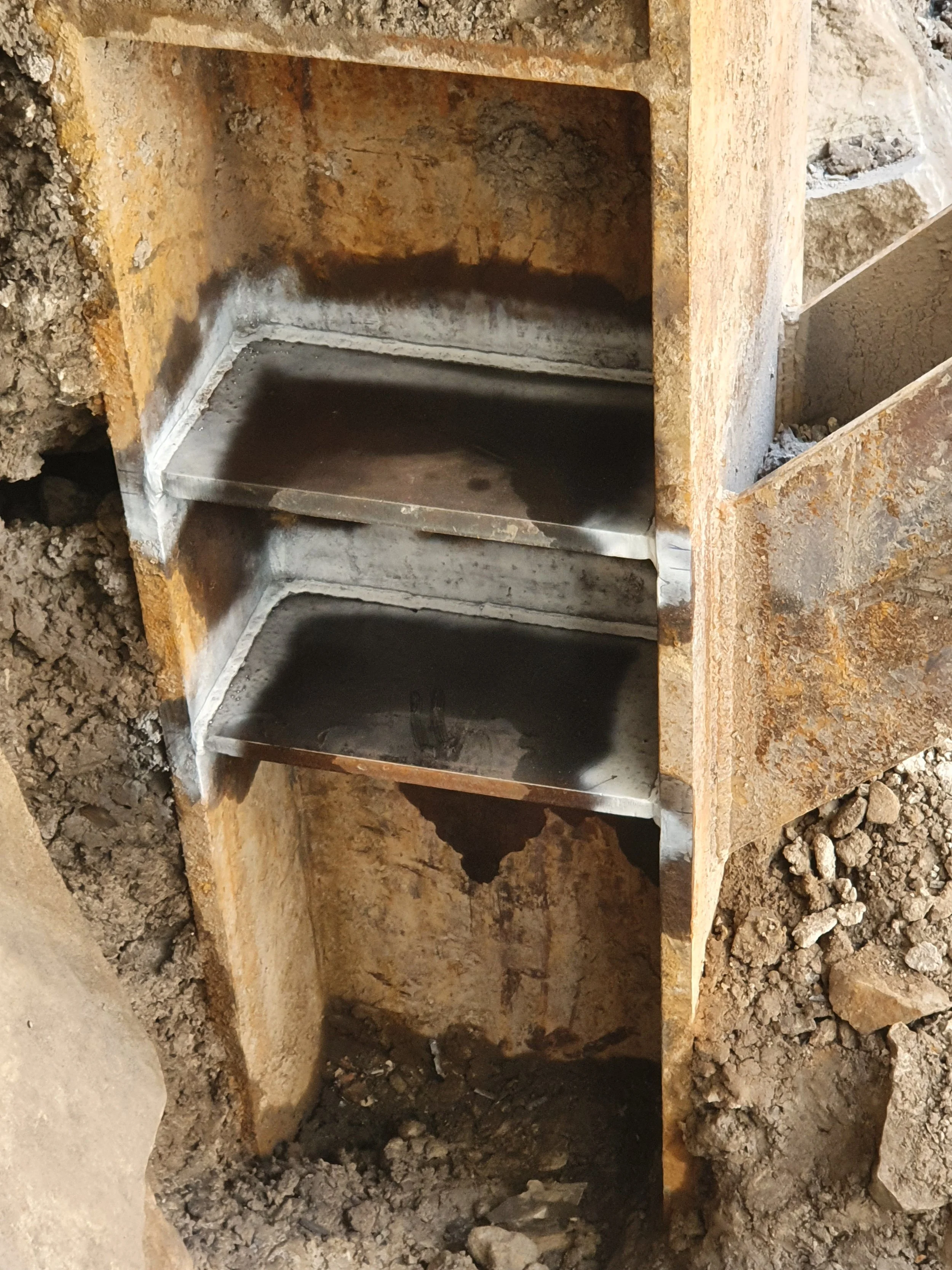 Close-up of a partially excavated old underground bank vault safe with rusted metal shelves inside, surrounded by dirt and rocks.