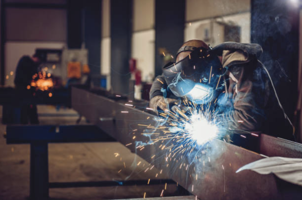 Worker welding metal with sparks flying inside a workshop.