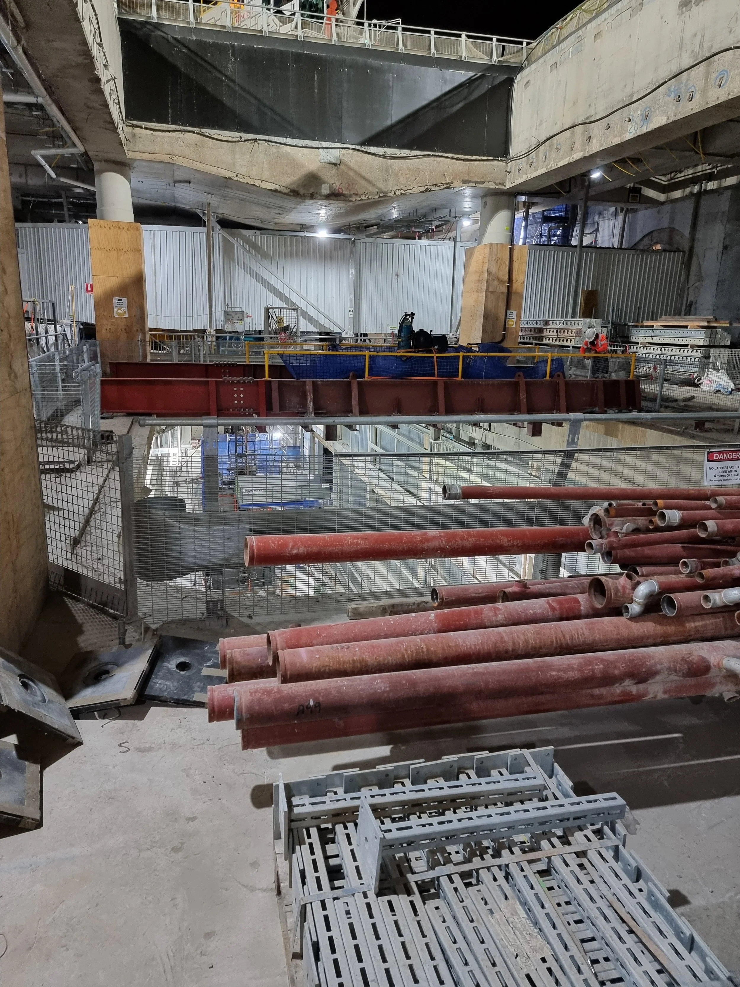 Construction site with metal pipes, scaffolding, and workers installing structures inside a multi-story building.