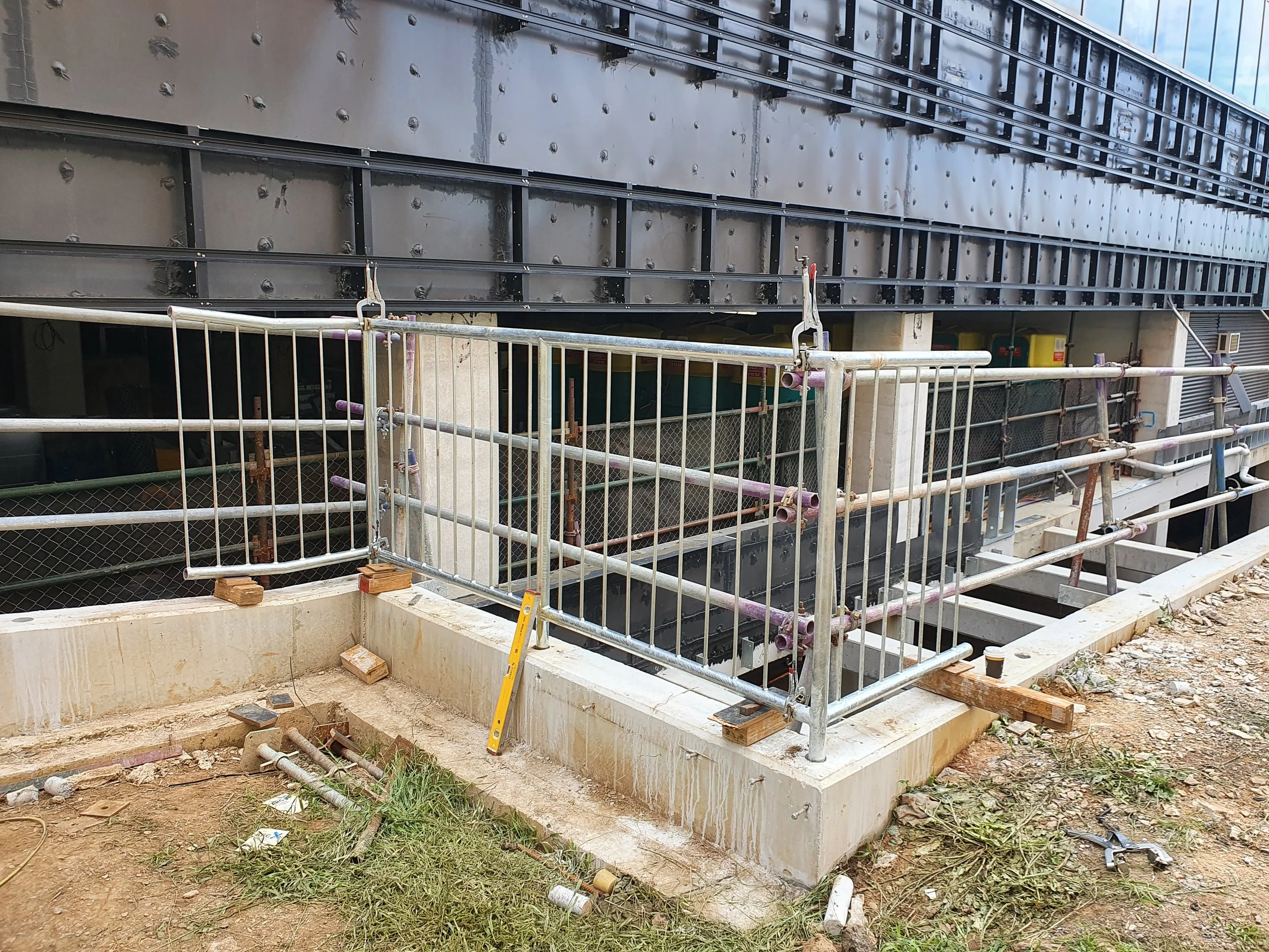 Construction site with metal fencing and scaffolding around a foundation, with tools and debris on the ground.