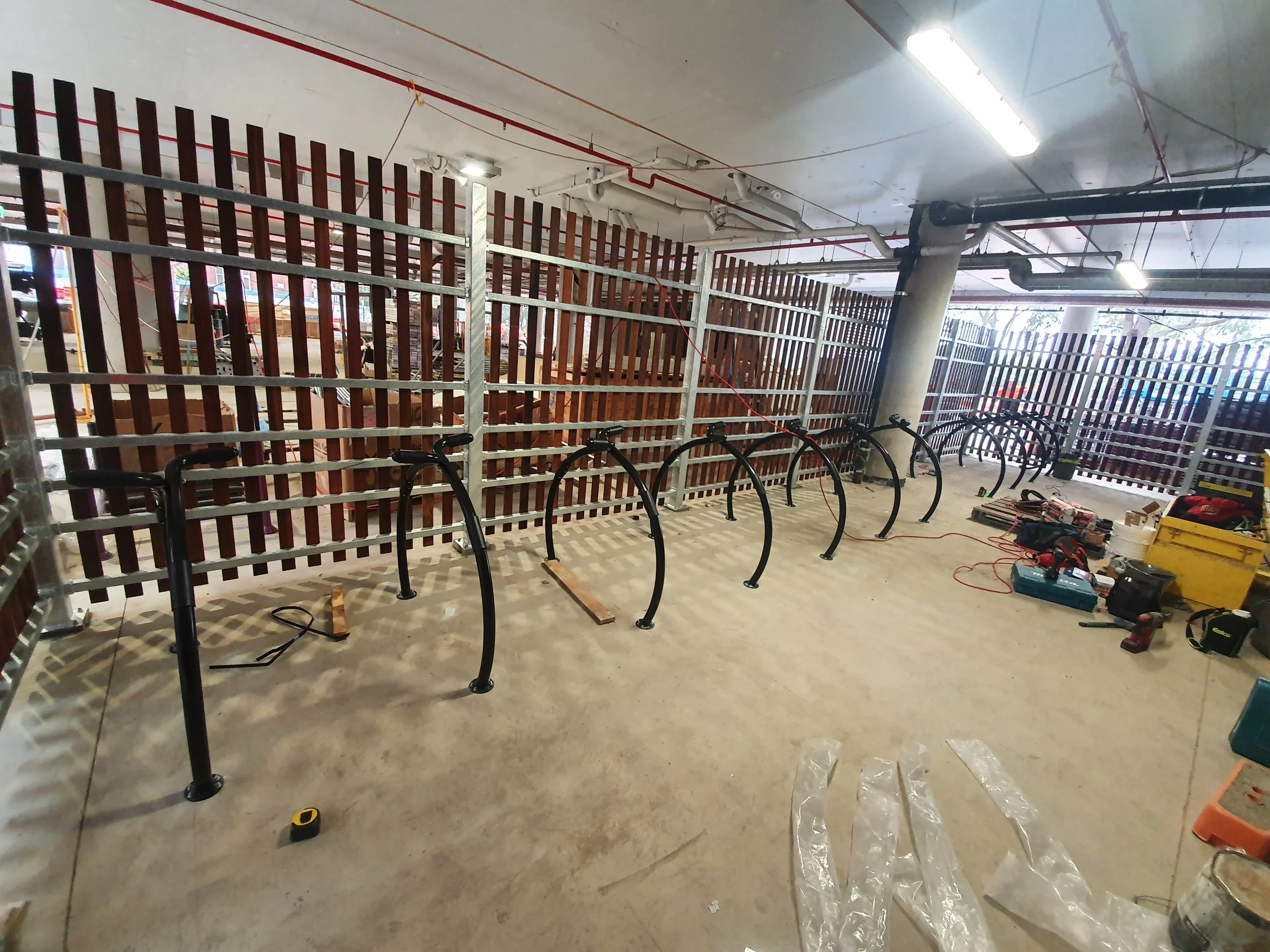Construction site with bicycle racks being installed inside a parking garage, tools and equipment scattered on the floor.