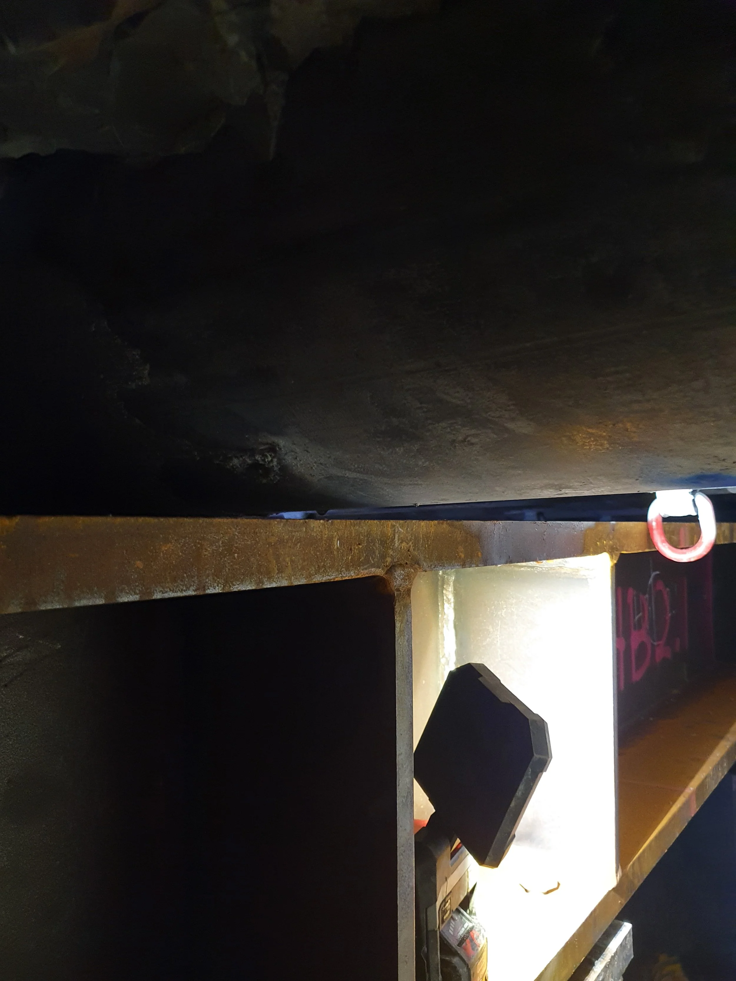 Close-up of a truck bed with a rusty metal edge, a small LED work light illuminating the area, and a piece of equipment or a part of a vehicle in the background.