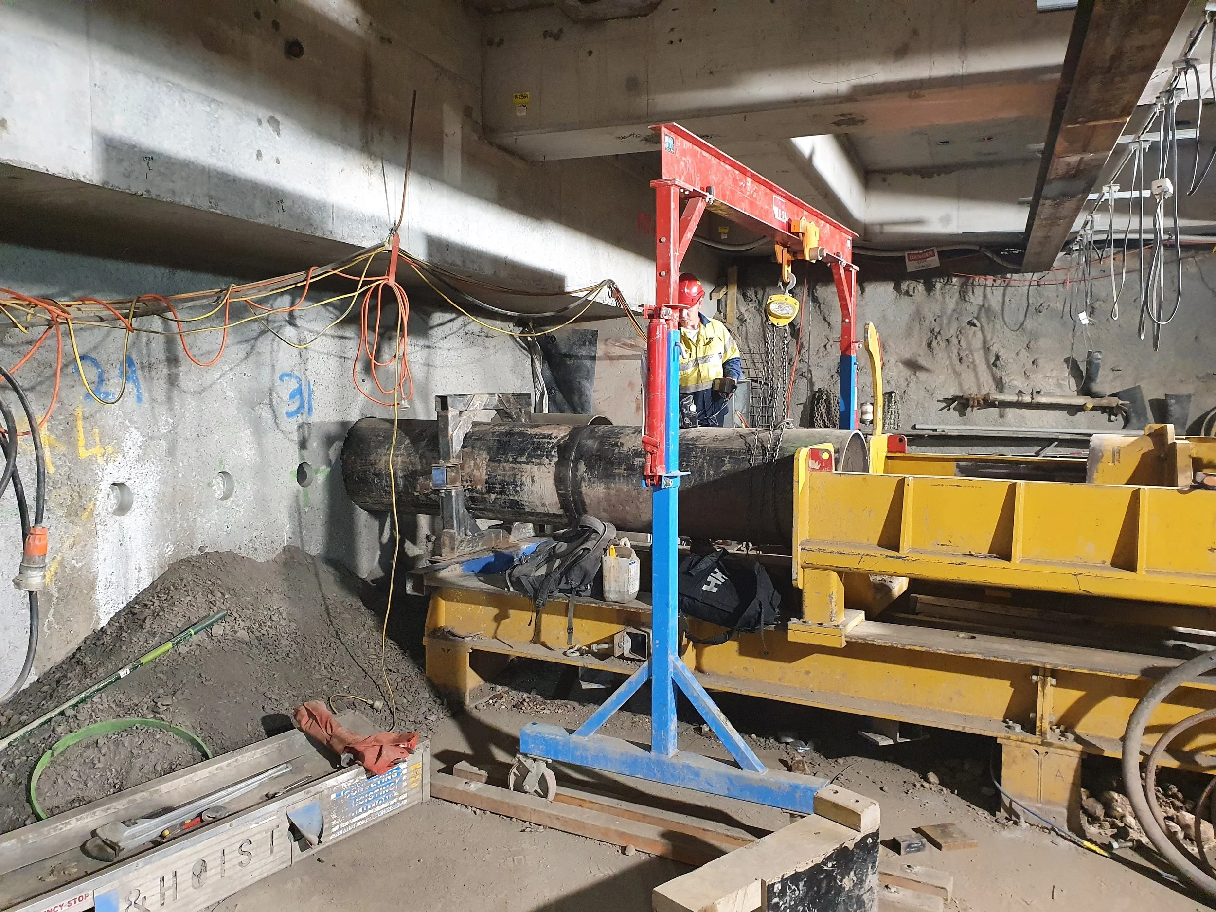 Construction worker in safety gear operating a large drilling machine inside a building under construction, surrounded by tools and wires.