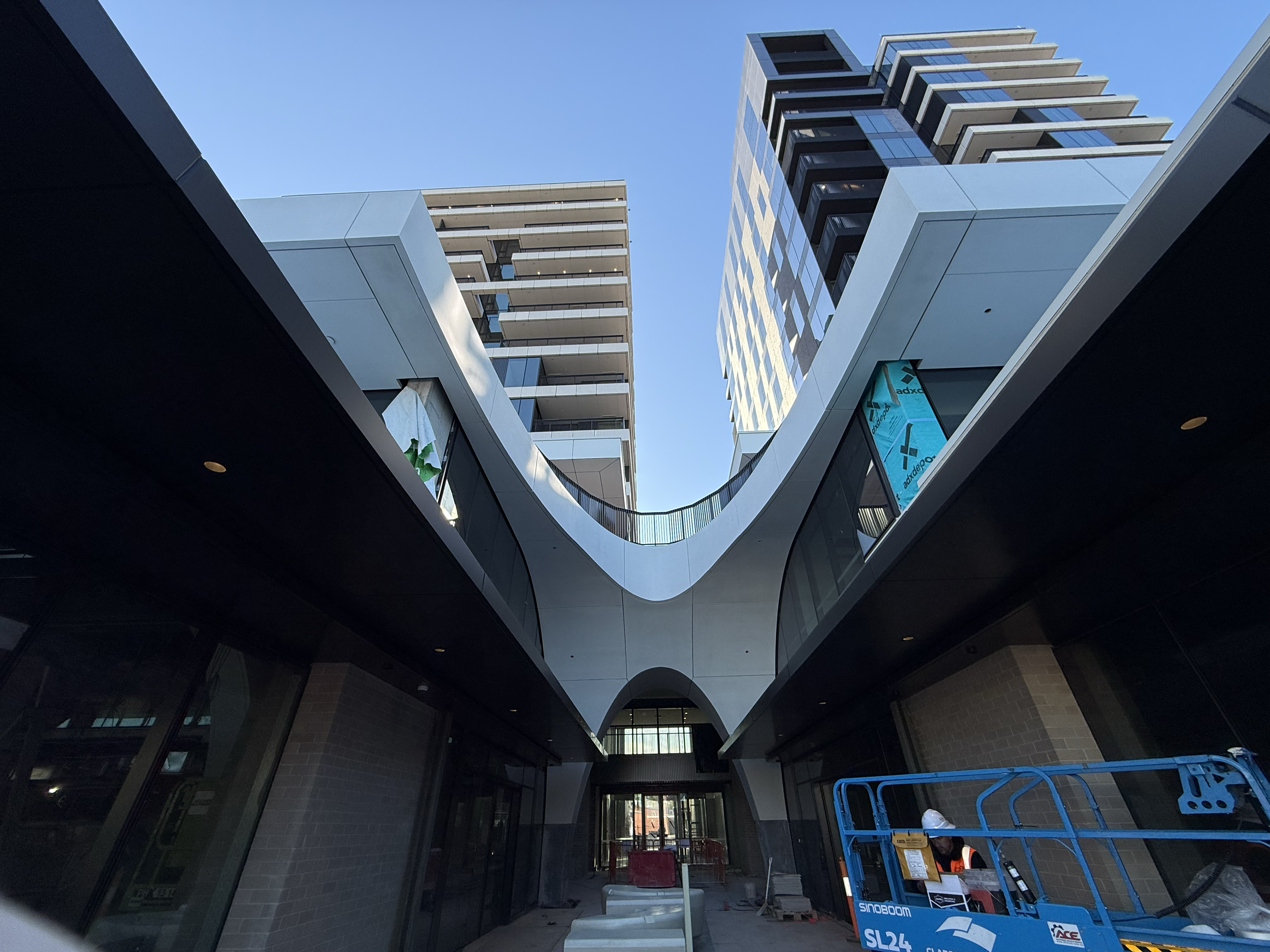 Modern architectural building with unique curved design, glass windows, and high-rise apartments on a clear blue sky day.