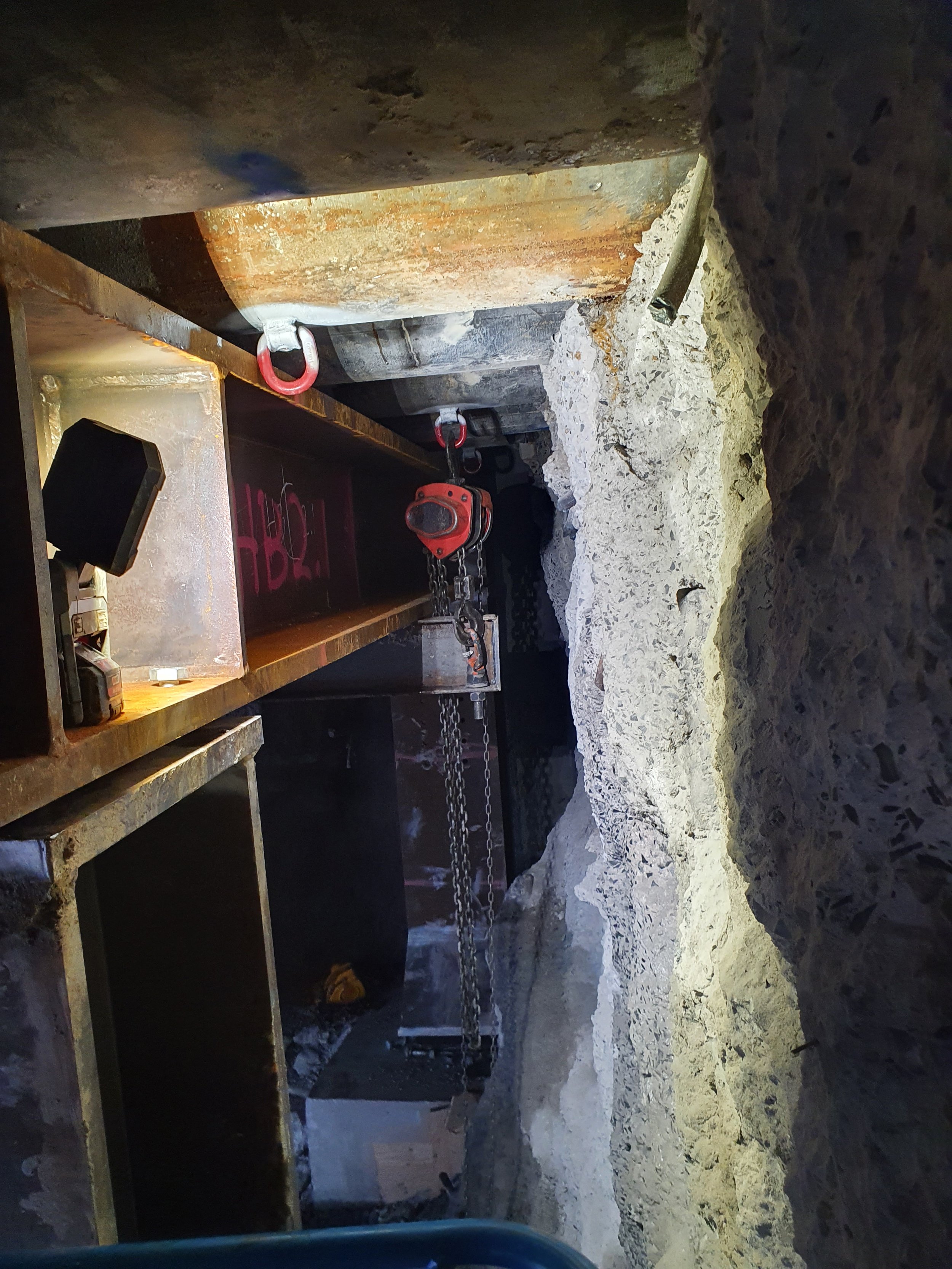 Construction site with large machinery, chains, and rocky walls, possibly an underground or tunnel excavation.