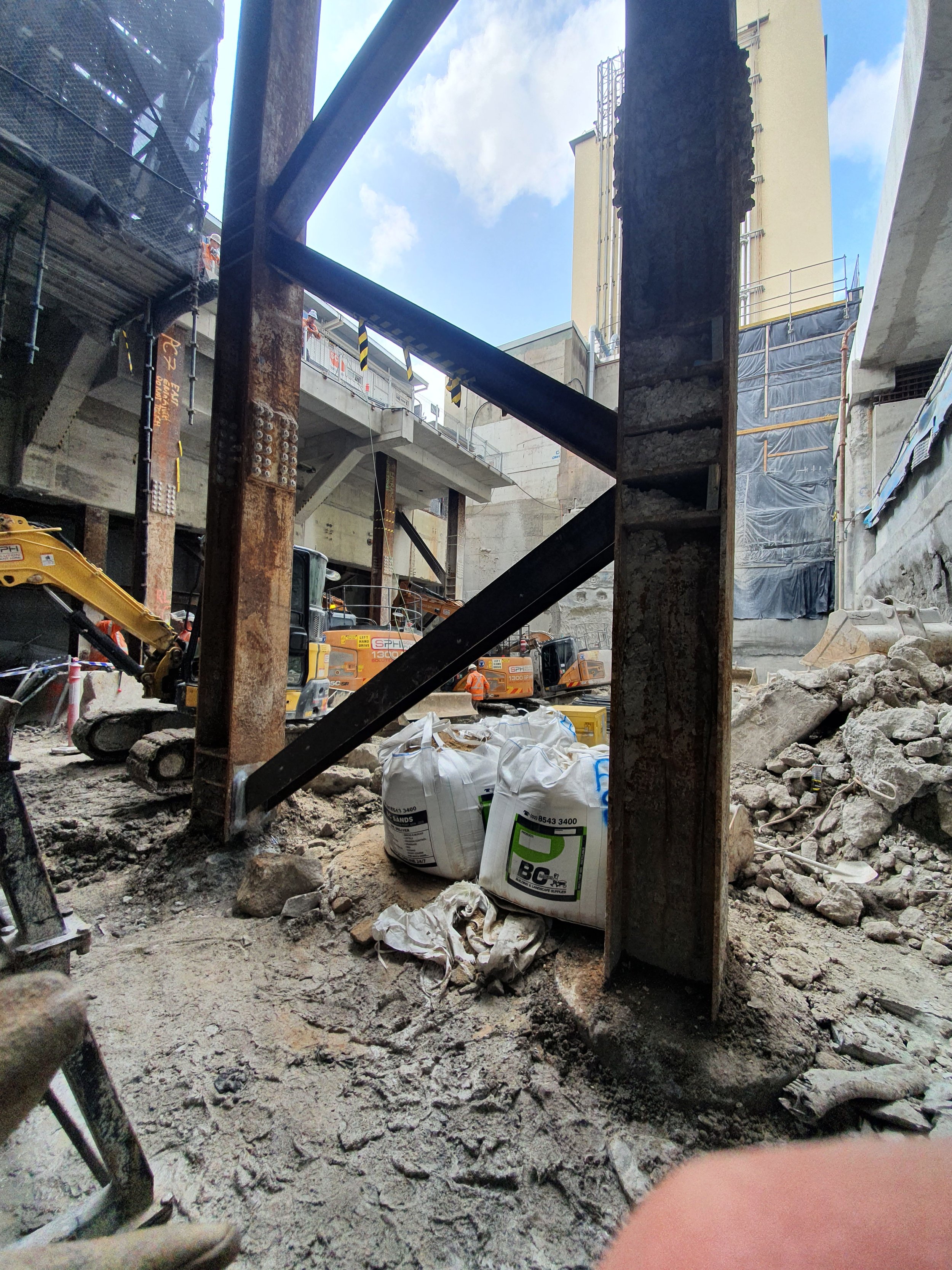 Construction site with construction equipment, debris, sandbags, scaffolding, and building under construction.