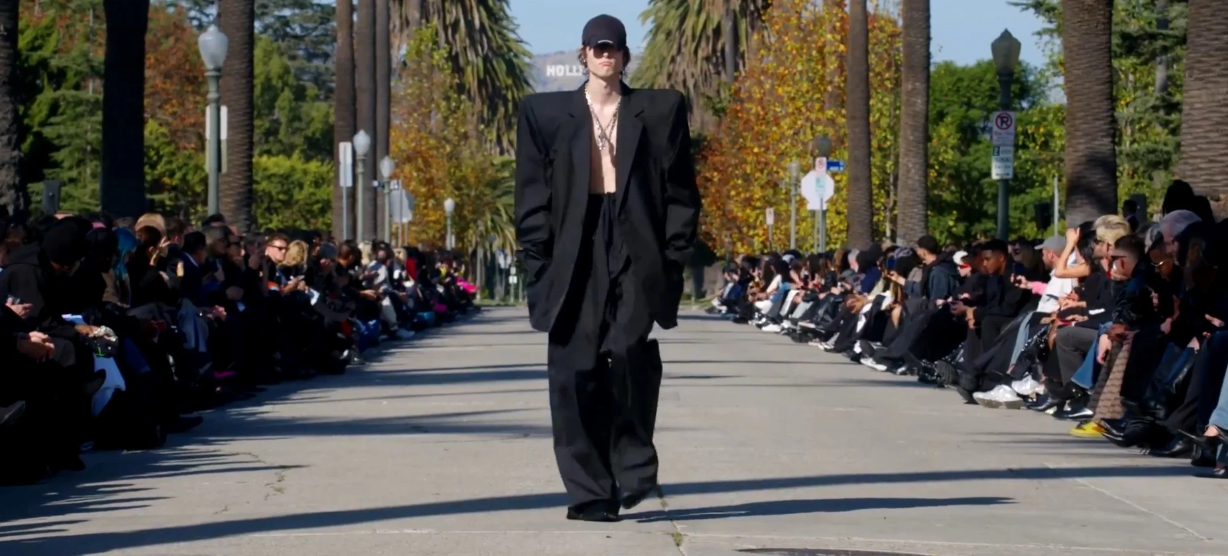 balenciaga-fall-2024-in-front-of-the-hollywood-sign,-a-model-on-the-runway-in-black-padded-blazer,-with-a-cap-and-high-waisted-boxy-oversized-trousers.jpg