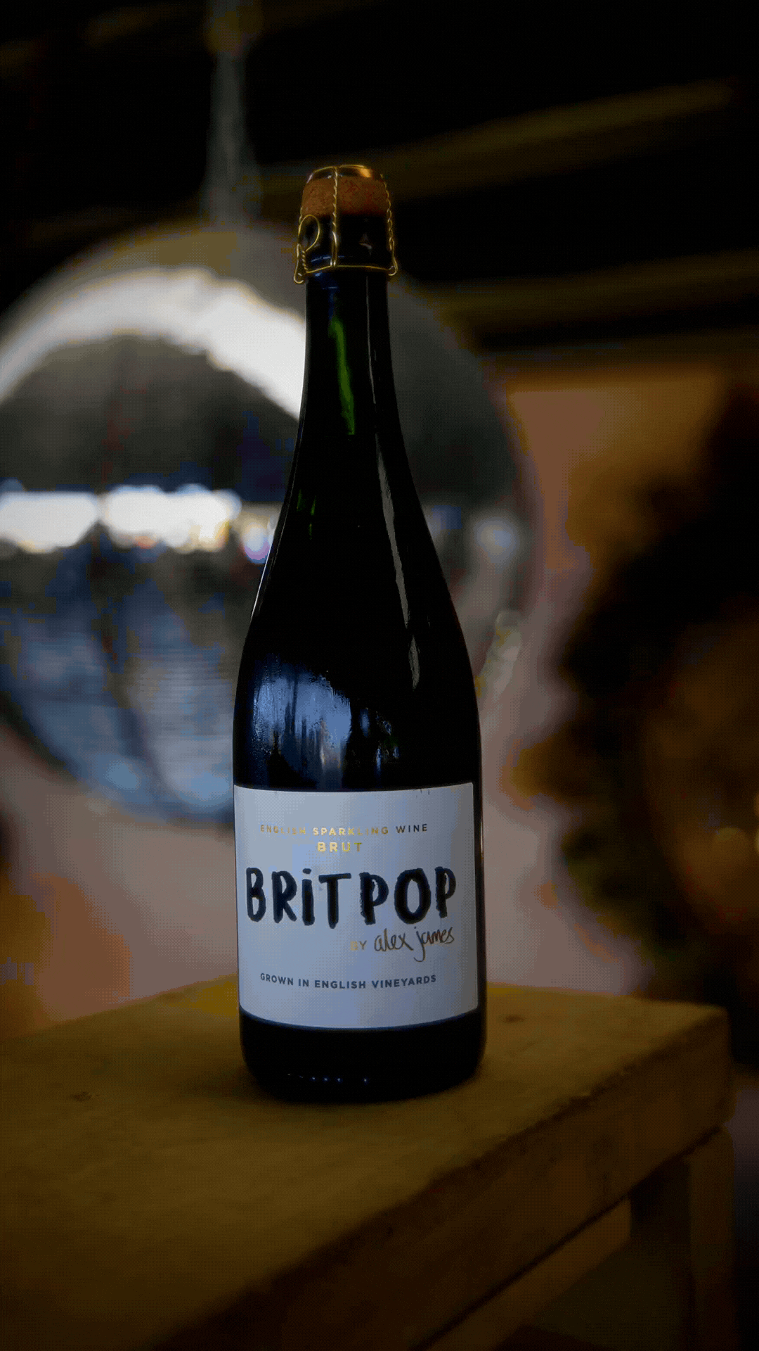 A dark glass bottle of BritPop sparkling wine with a white label, placed on a wooden surface with a blurry background.