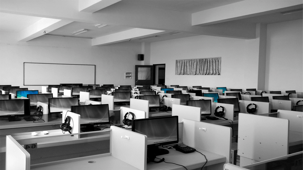 Empty computer lab with multiple workstations, monitors, and headsets.