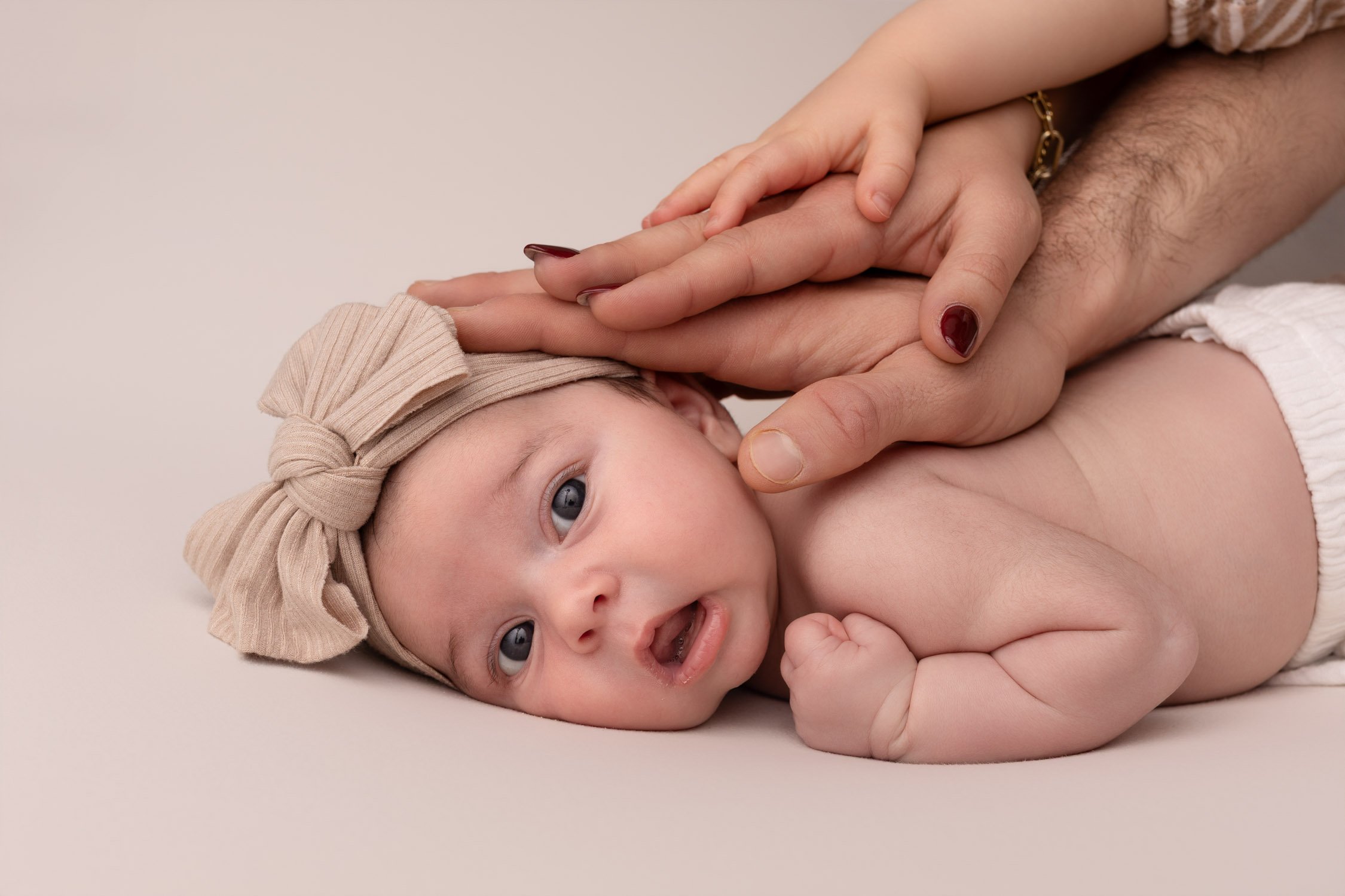 Séance photo naissance Yvelines - bébé éveillé sur le ventre avec les mains de son papa, sa maman et sa grande soeur 