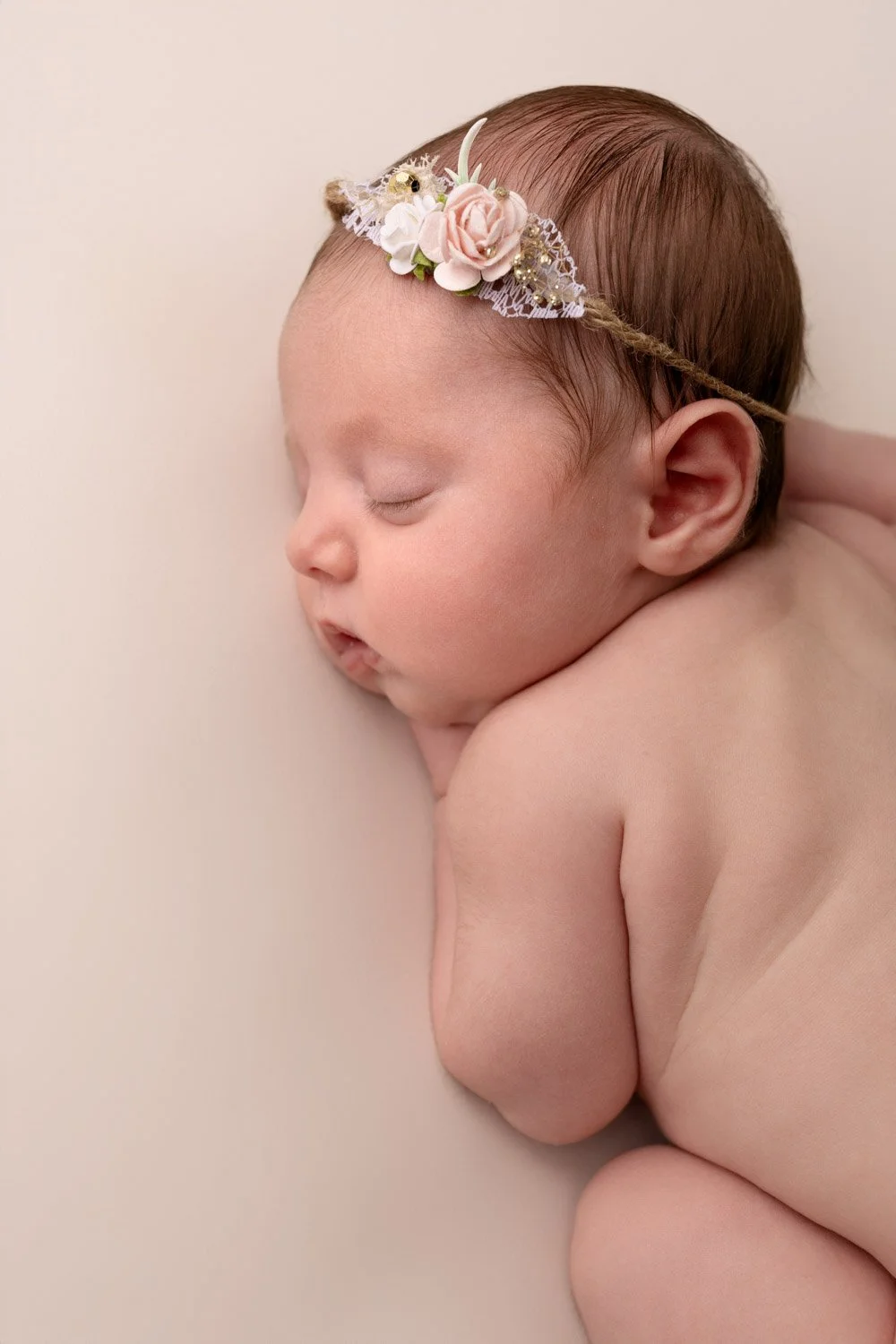 Séance photo naissance Yvelines - bébé à plat ventre avec bandeau fleuri sur la tête 