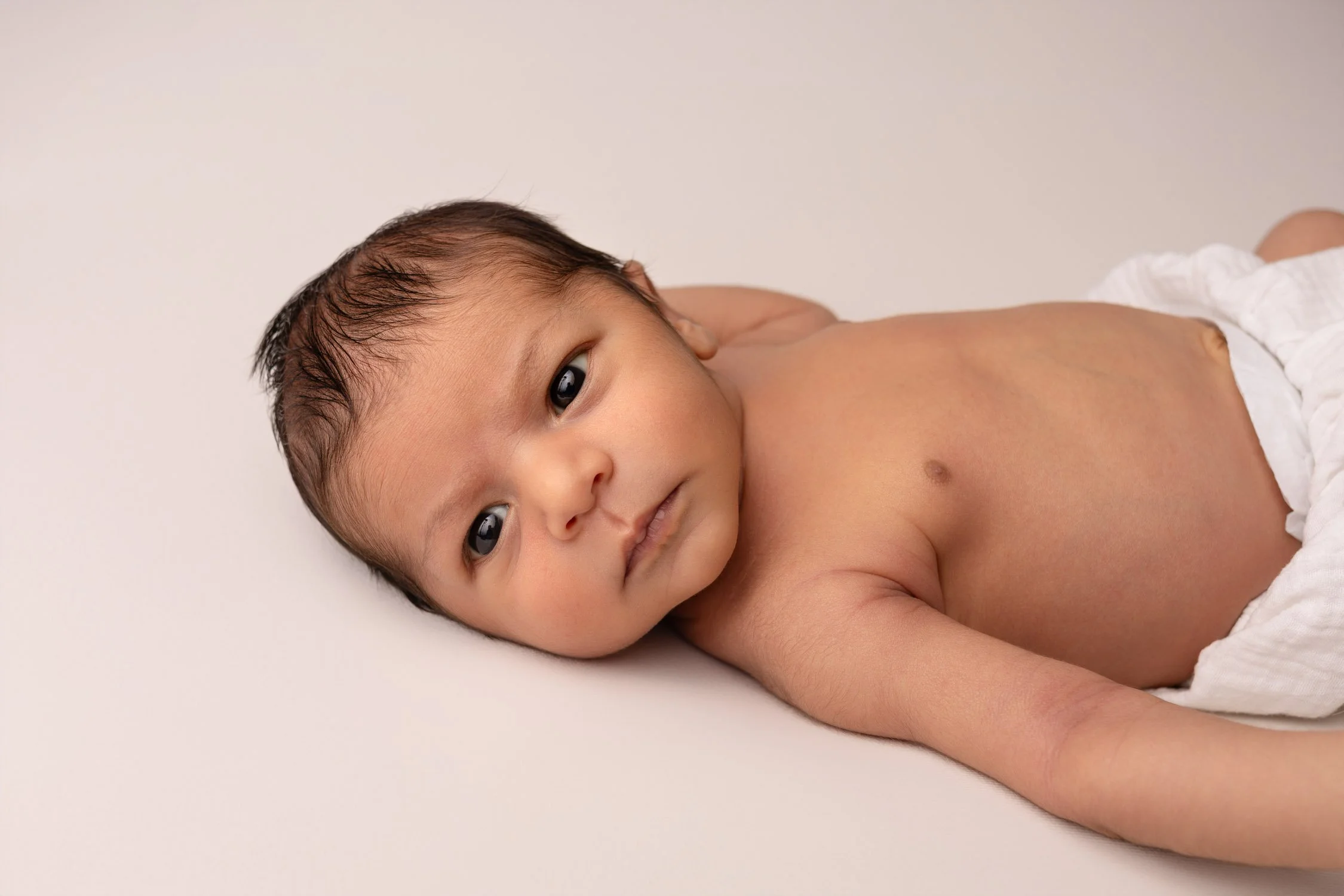 Séance photo naissance Yvelines - bébé éveillé sur le dos regard vers l'appareil 