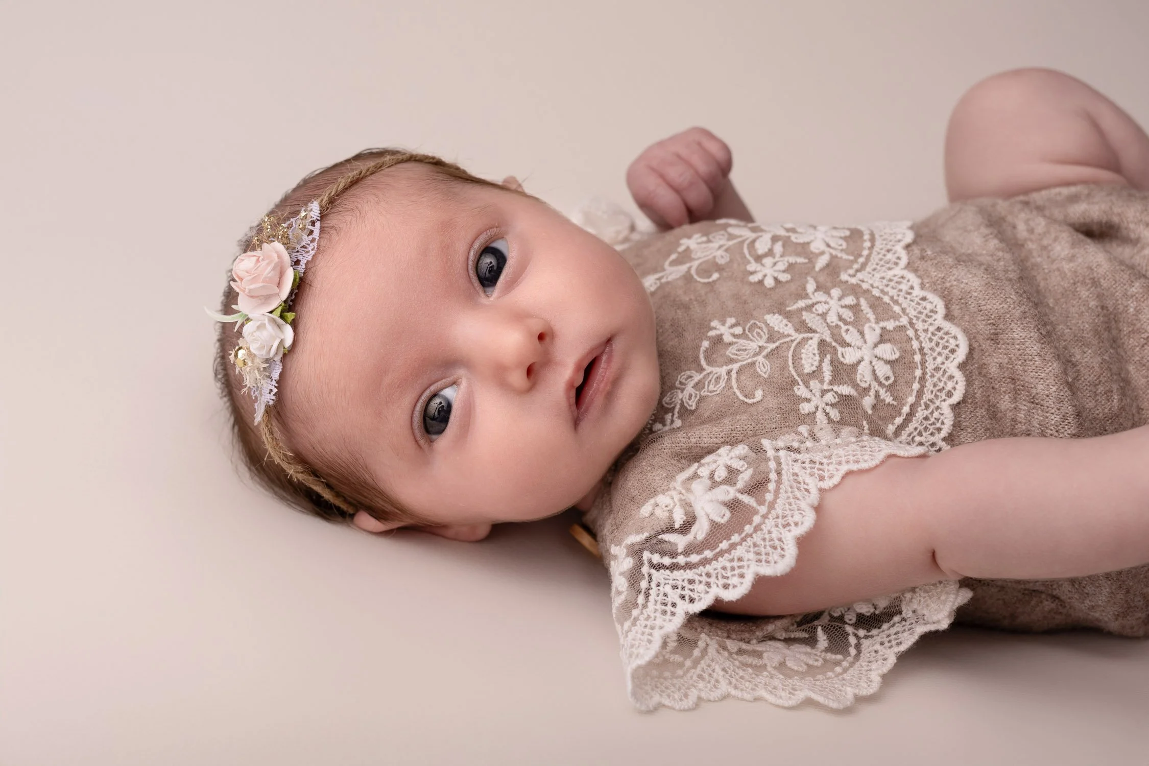 Séance photo naissance Yvelines - bébé allongé éveillé regard vers l'appareil, petite tenue beige dentelle