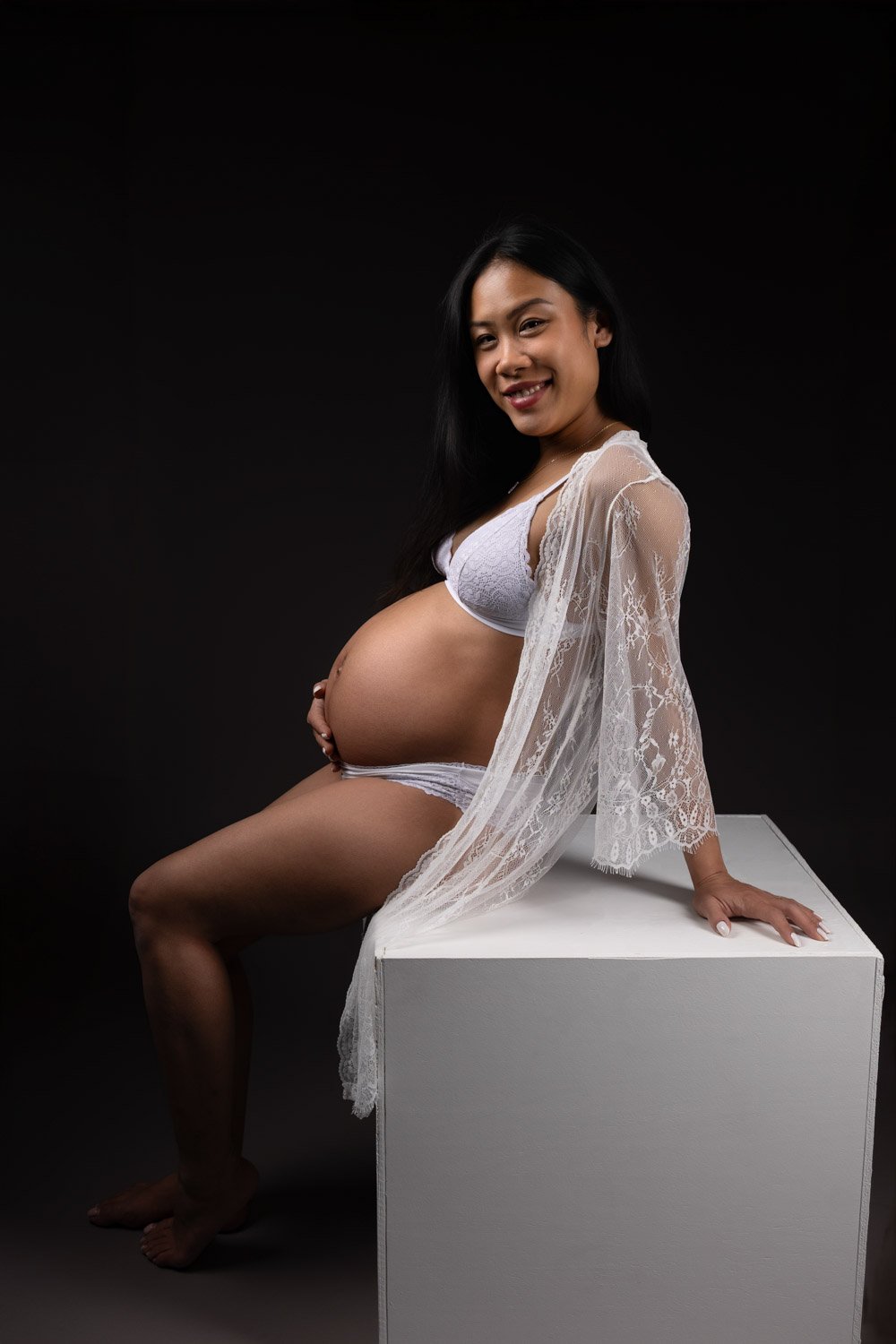 Séance photo grossesse Yvelines - future maman assise sur un cube, habillé en blanc, clair obscur 