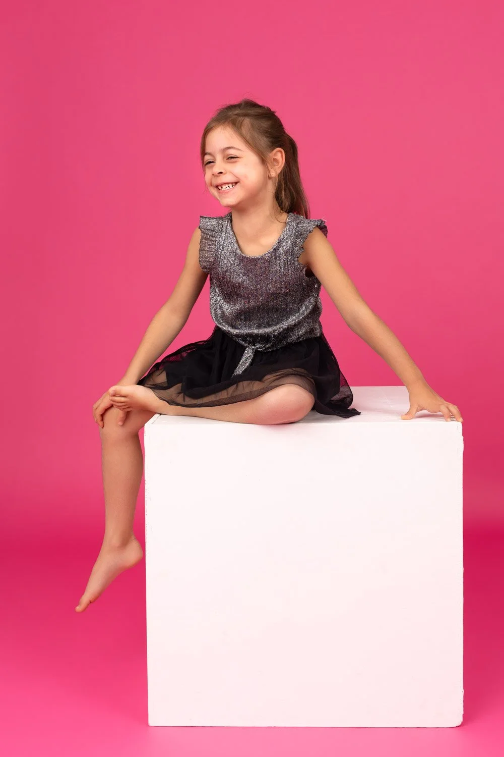 Petite fille de 6 ans assise sur un cube fond rose pétant