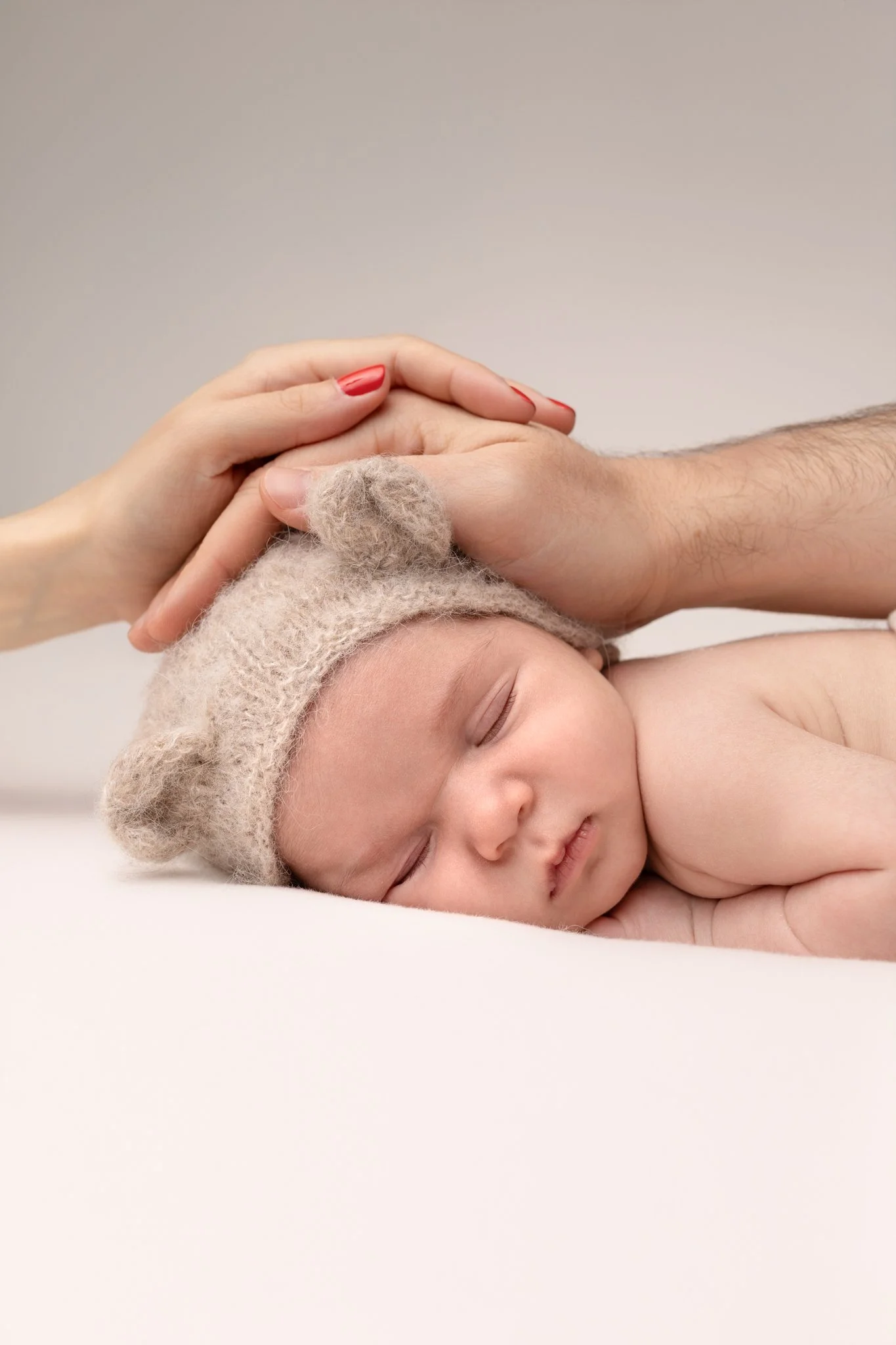 Séance photo naissance Yvelines - bébé endormi bonnet ourson avec mains des parents sur la tête 
