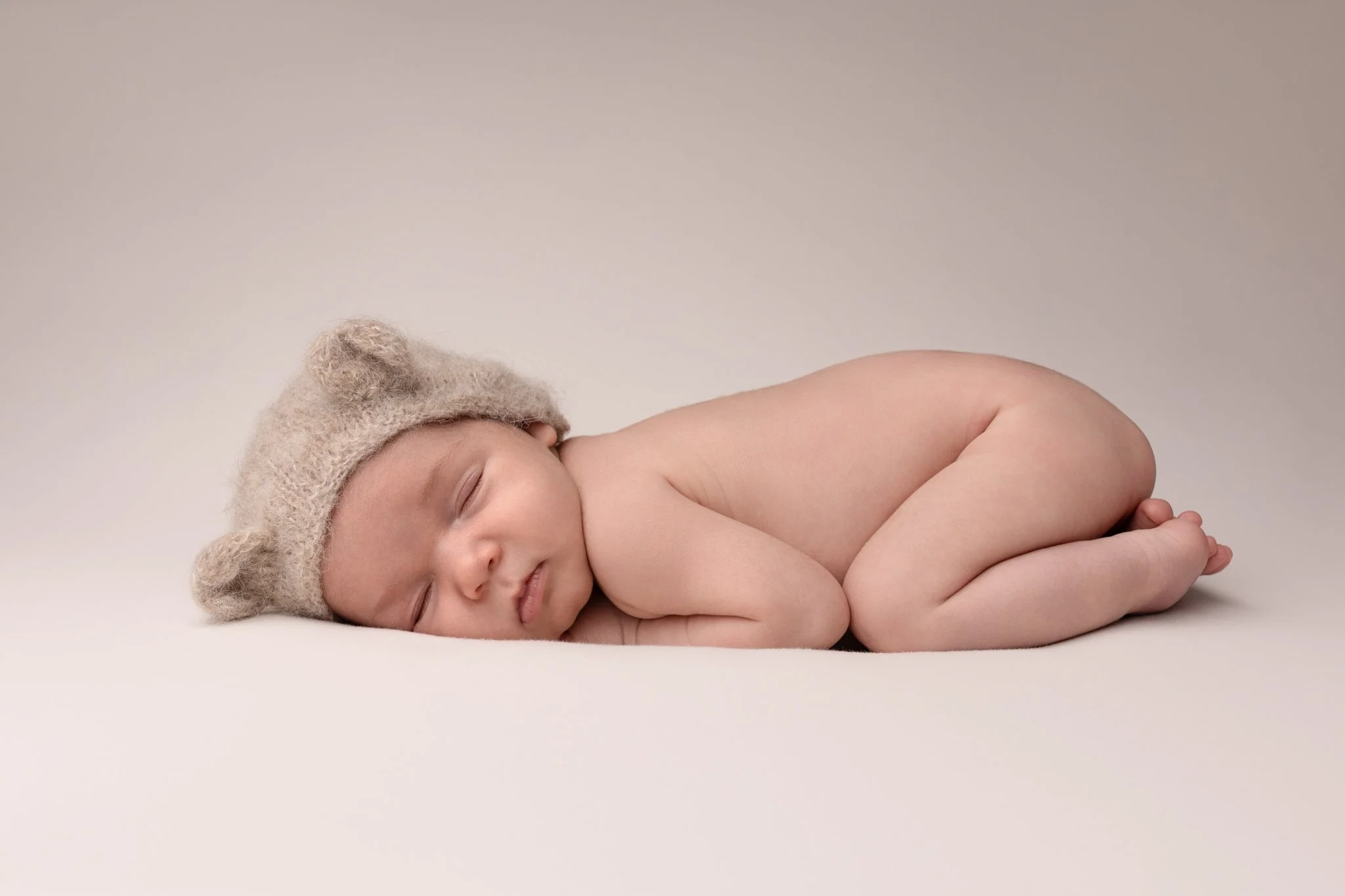 Séance photo naissance Yvelines - bébé endormi à plat ventre avec bonnet ourson et tout nu