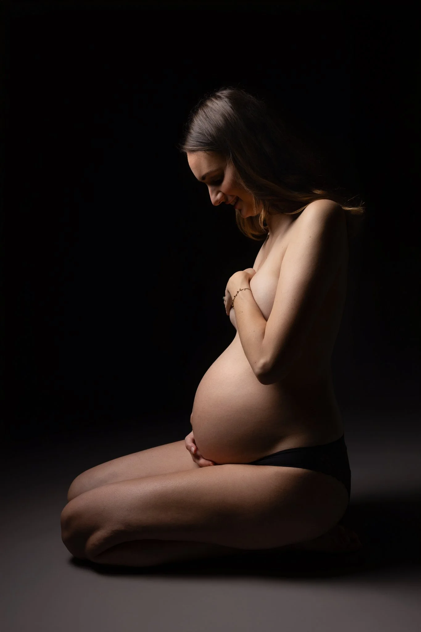Séance photo grossesse Yvelines - future maman en clair obscur, mains cachant la poitrine, ventre nu, à genoux