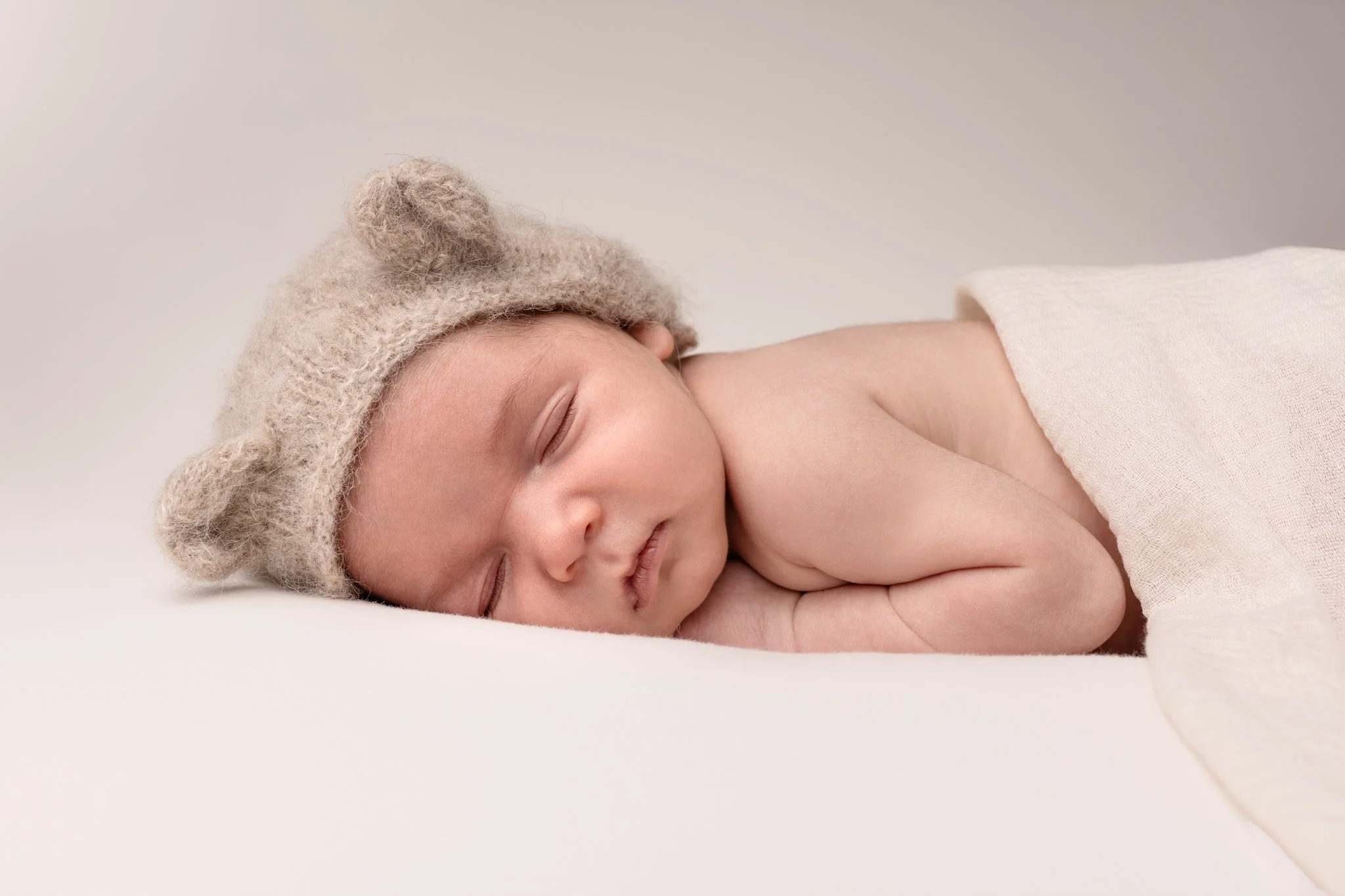 Séance photo naissance Yvelines - bébé endormi à plat ventre avec bonnet ourson et lange