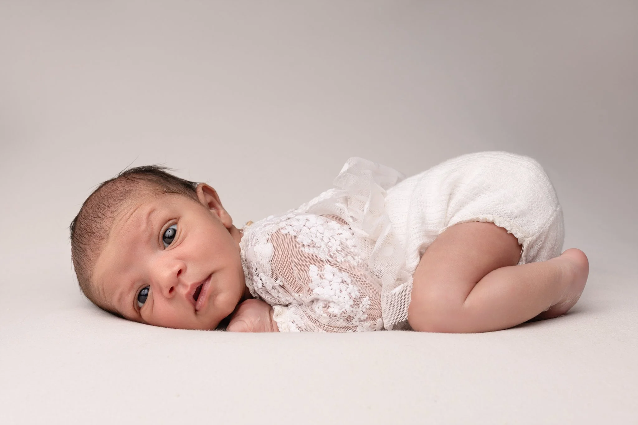 Séance photo naissance Yvelines - bébé éveillé sur le ventre avec petite tenue en dentelle