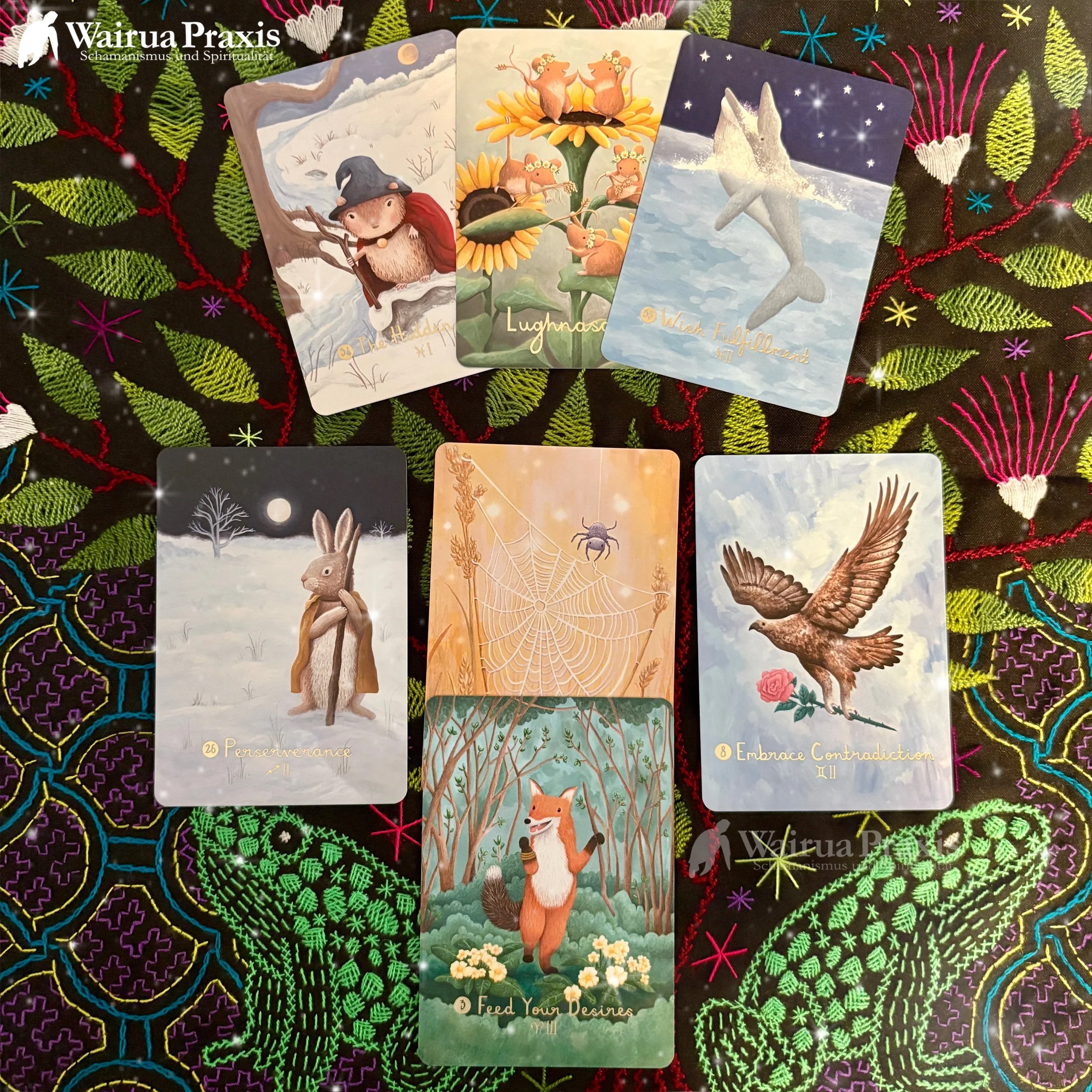 Sieben Tarotkarten mit symbolischen Motiven auf einem bunten bestickten Stoff.