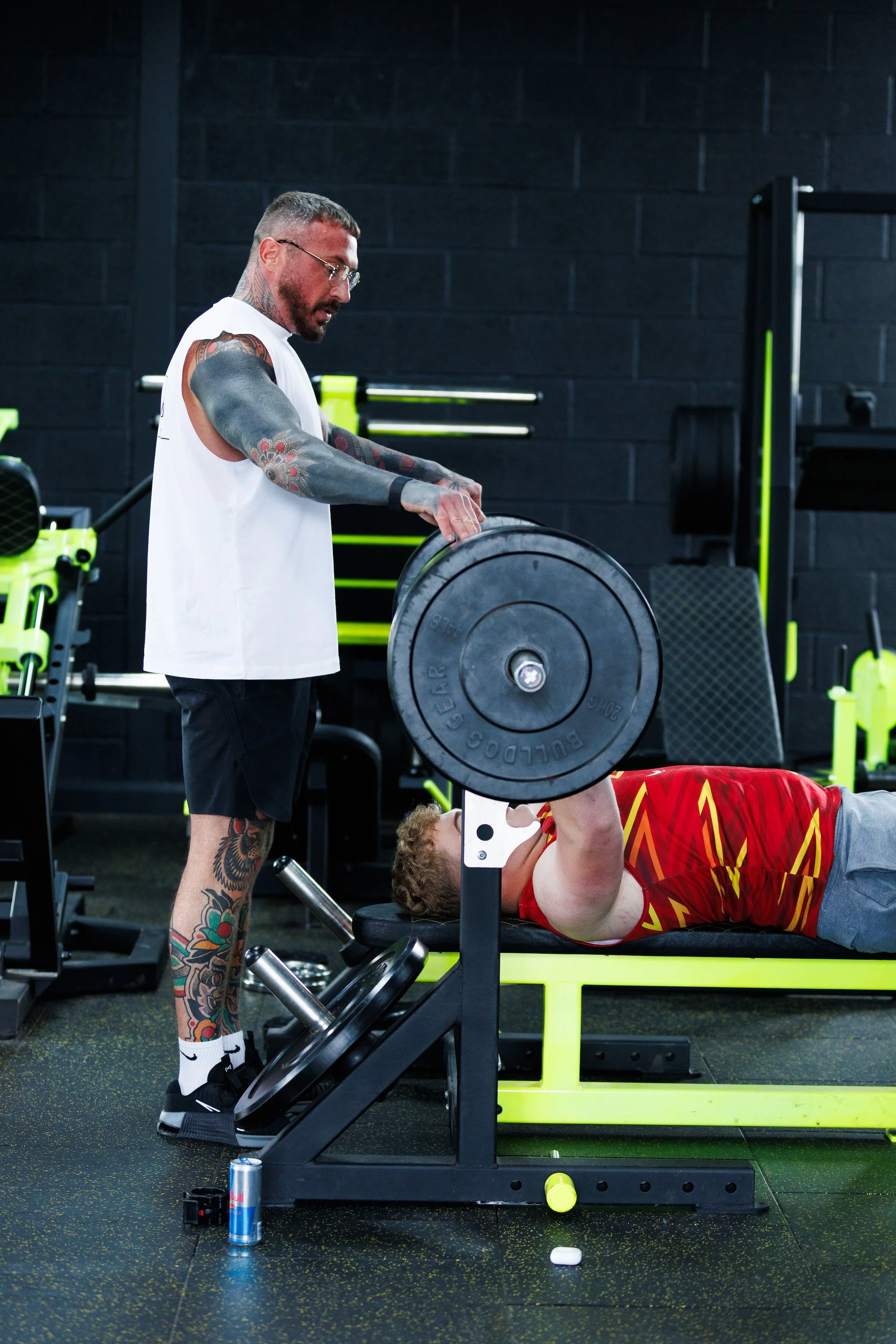 A personal trainer is spotting a client as he lifts weights on a bench at Alpha Athletic Gym.