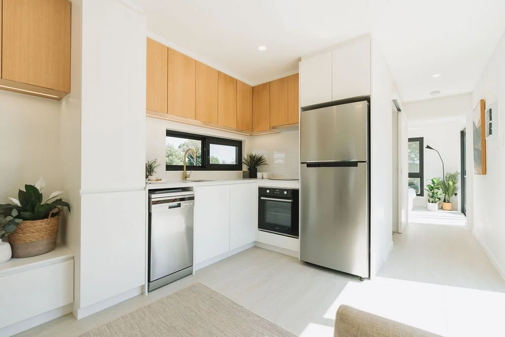 A bright and modern kitchen space, looking down a hallway towards a bedroom