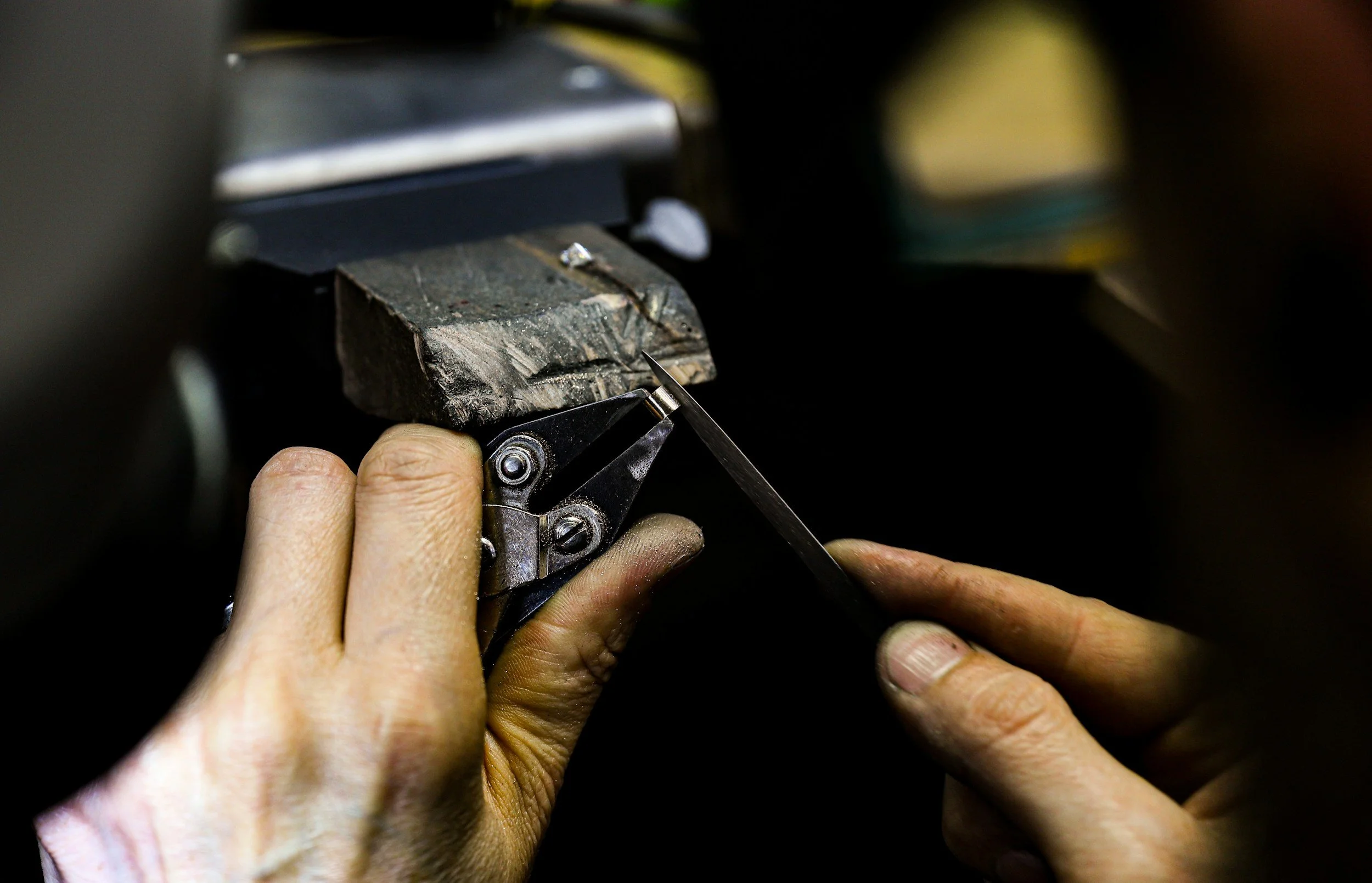 Close-up of a person's hands sharpening a small blade on a grinding stone.