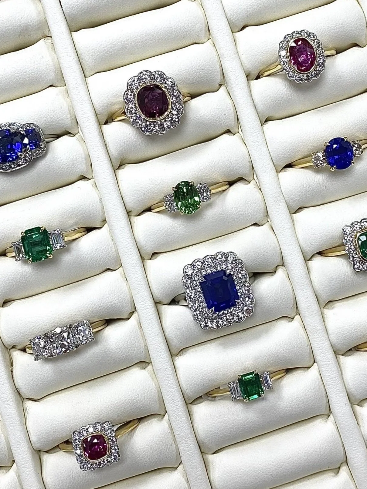 Collection of gold rings with colored gemstones and diamonds on a white jewelry display.