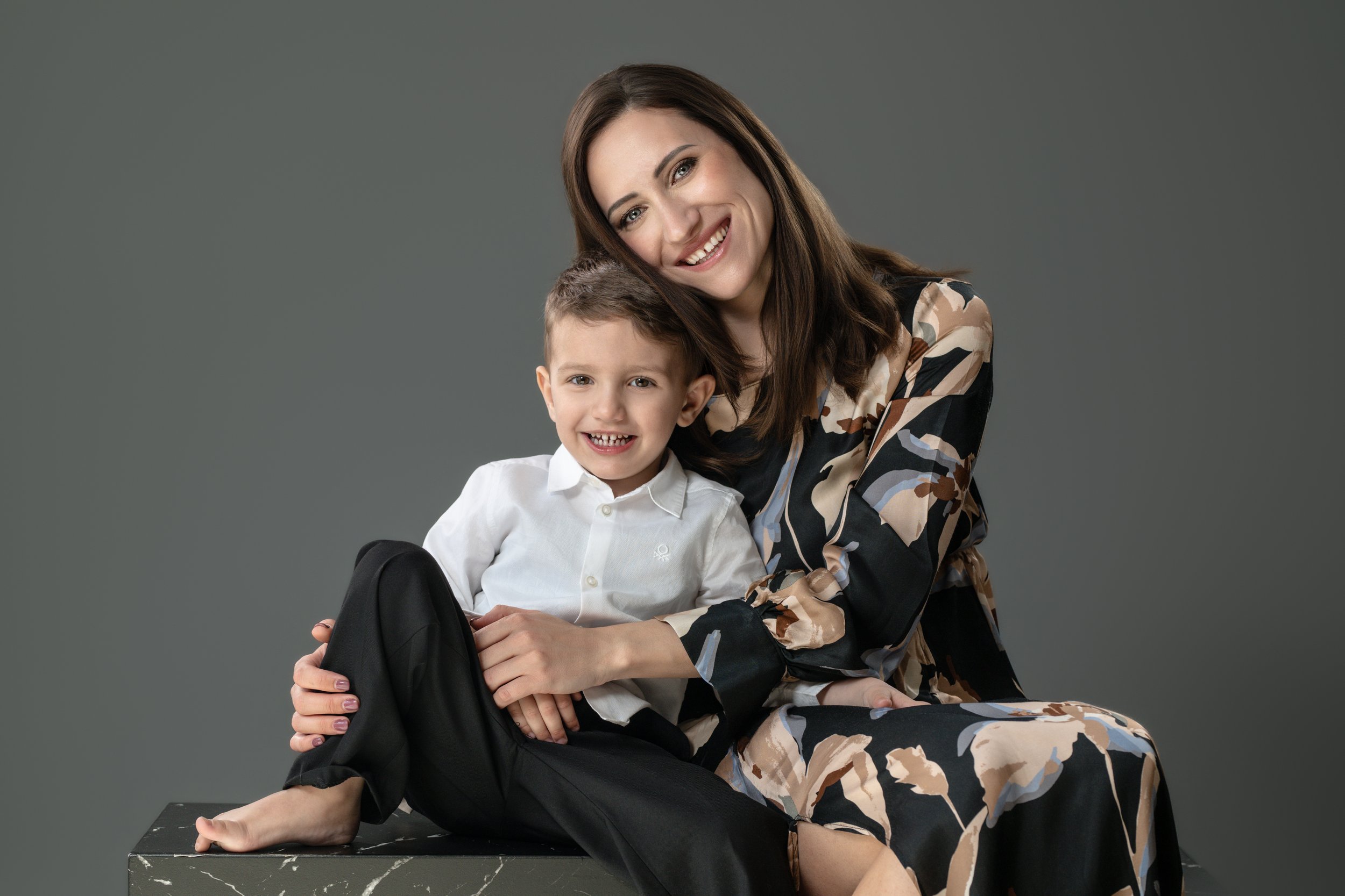Una donna sorridente e un bambino seduti insieme, entrambi guardano verso la fotocamera.