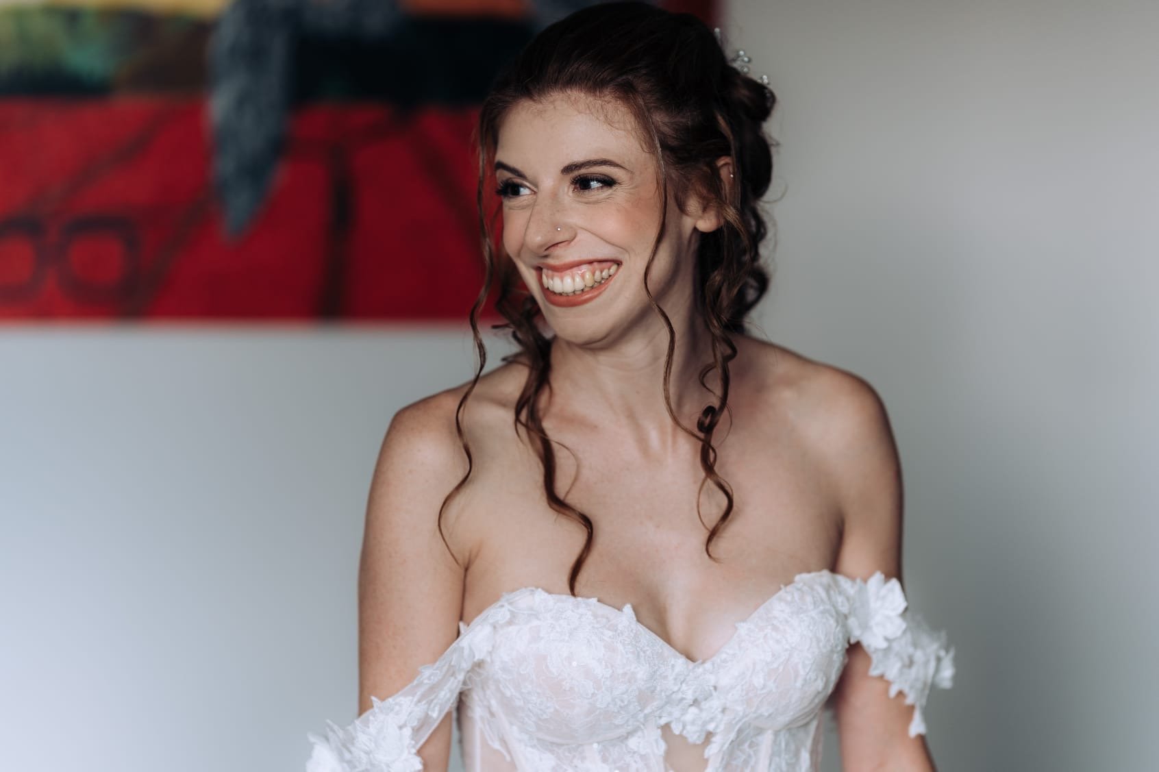 Una donna sorridente in abito da sposa bianco con un quadro astratto sullo sfondo.