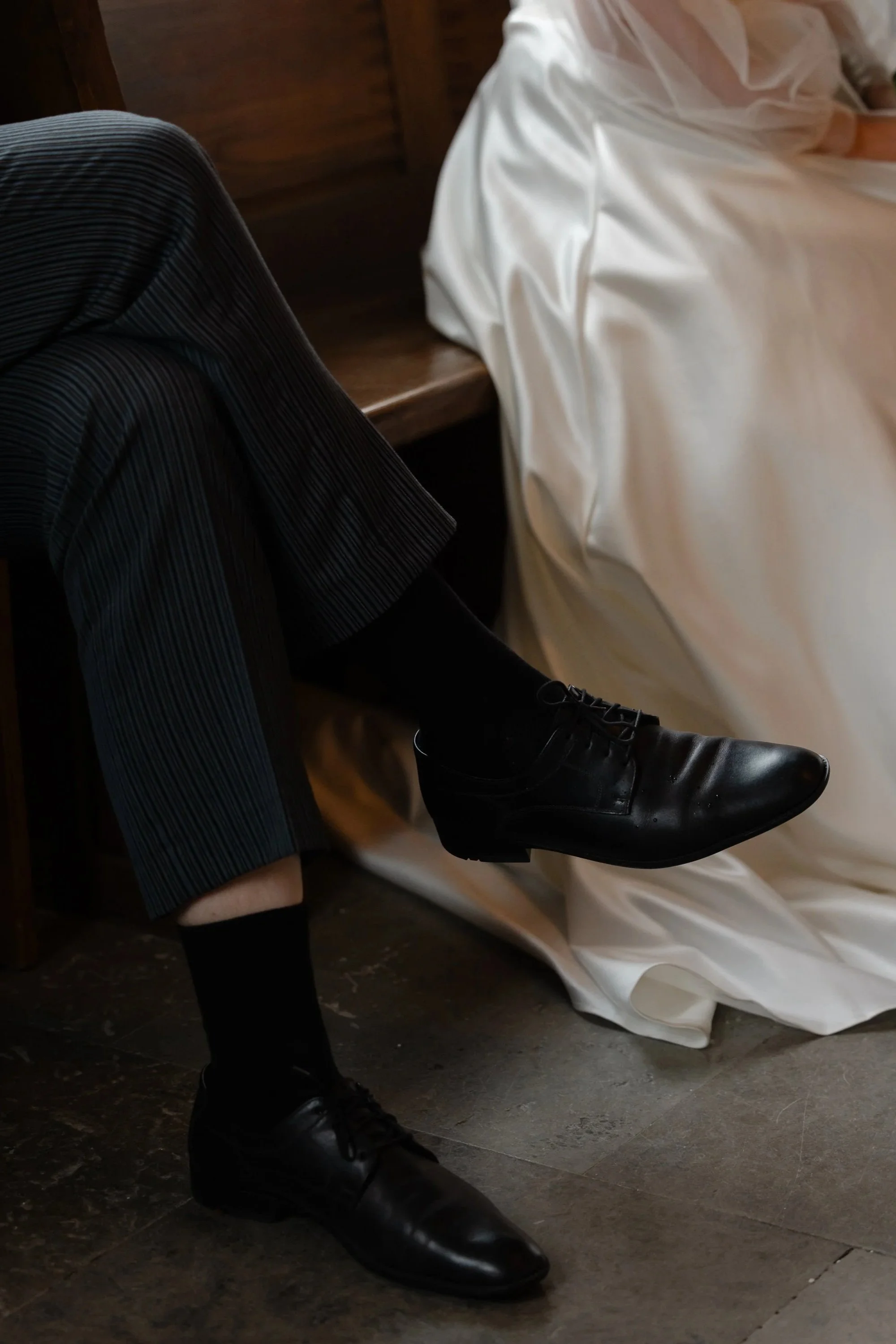 Mörk bild med atmosfär och editorial stil, brudgummens ben och en del av brudens klänning syns.