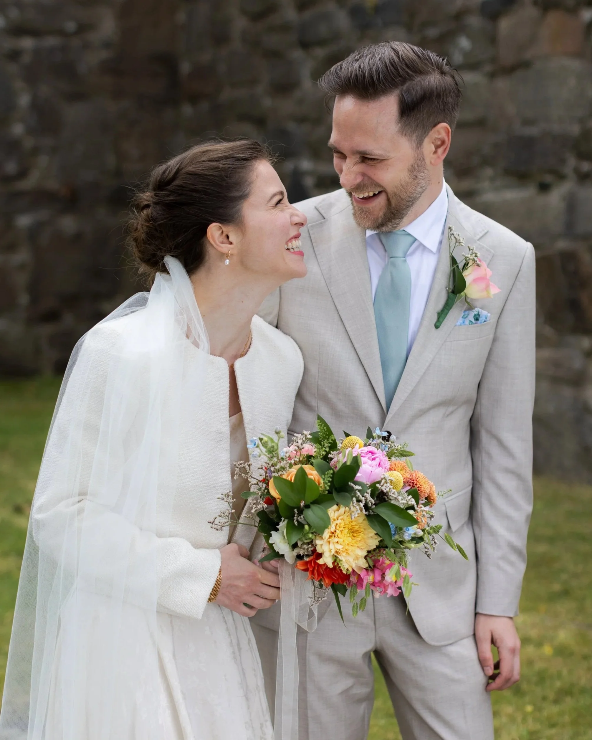 ungt brudpar skrattar högt och tittar på varandra, bruden håller en vacker bukett