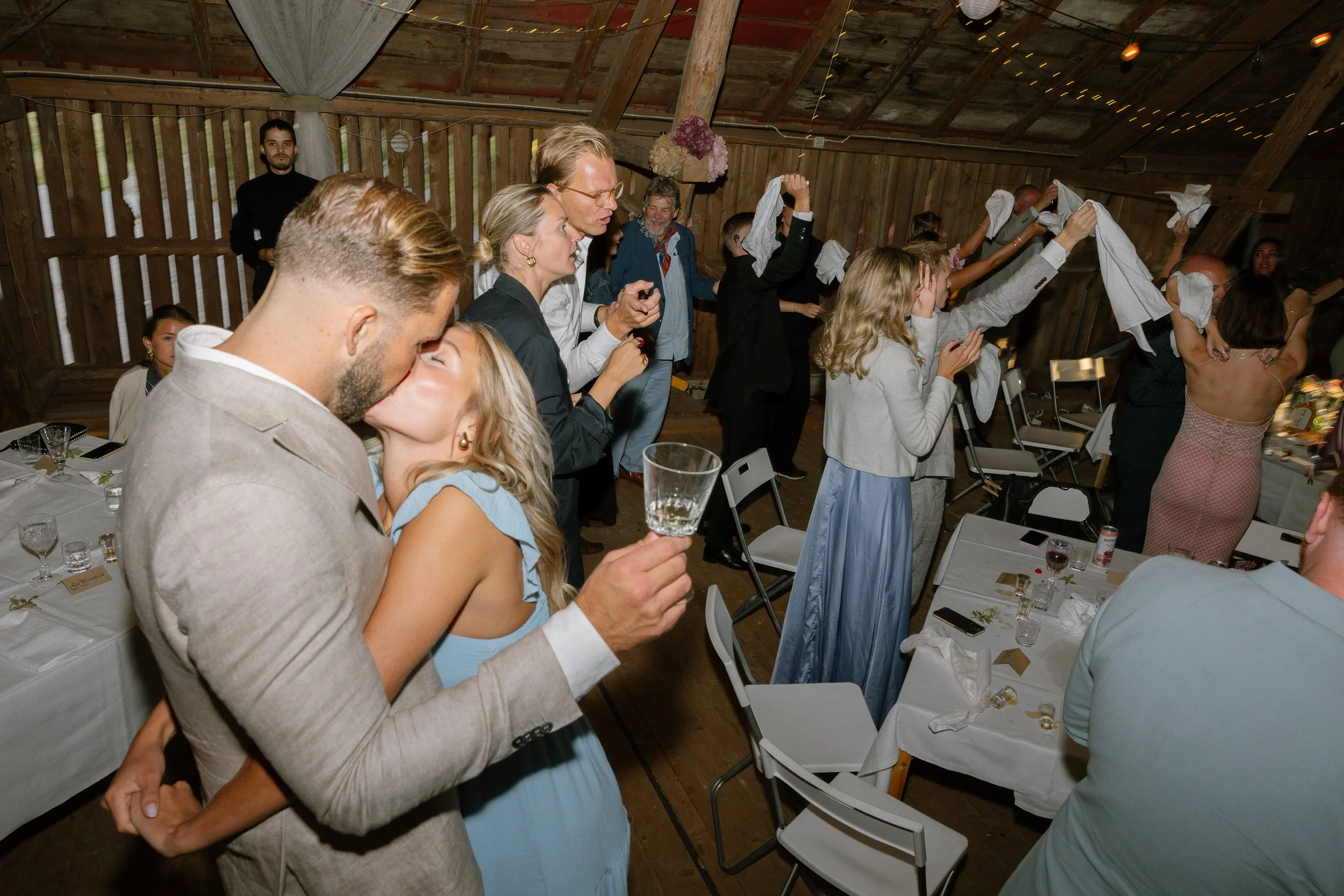 En grupp människor som deltar i en fest dansar och firar, några håller vita servetter i luften.  Av Sofia Wilhelmina bröllopsfotograf i Stockholm.