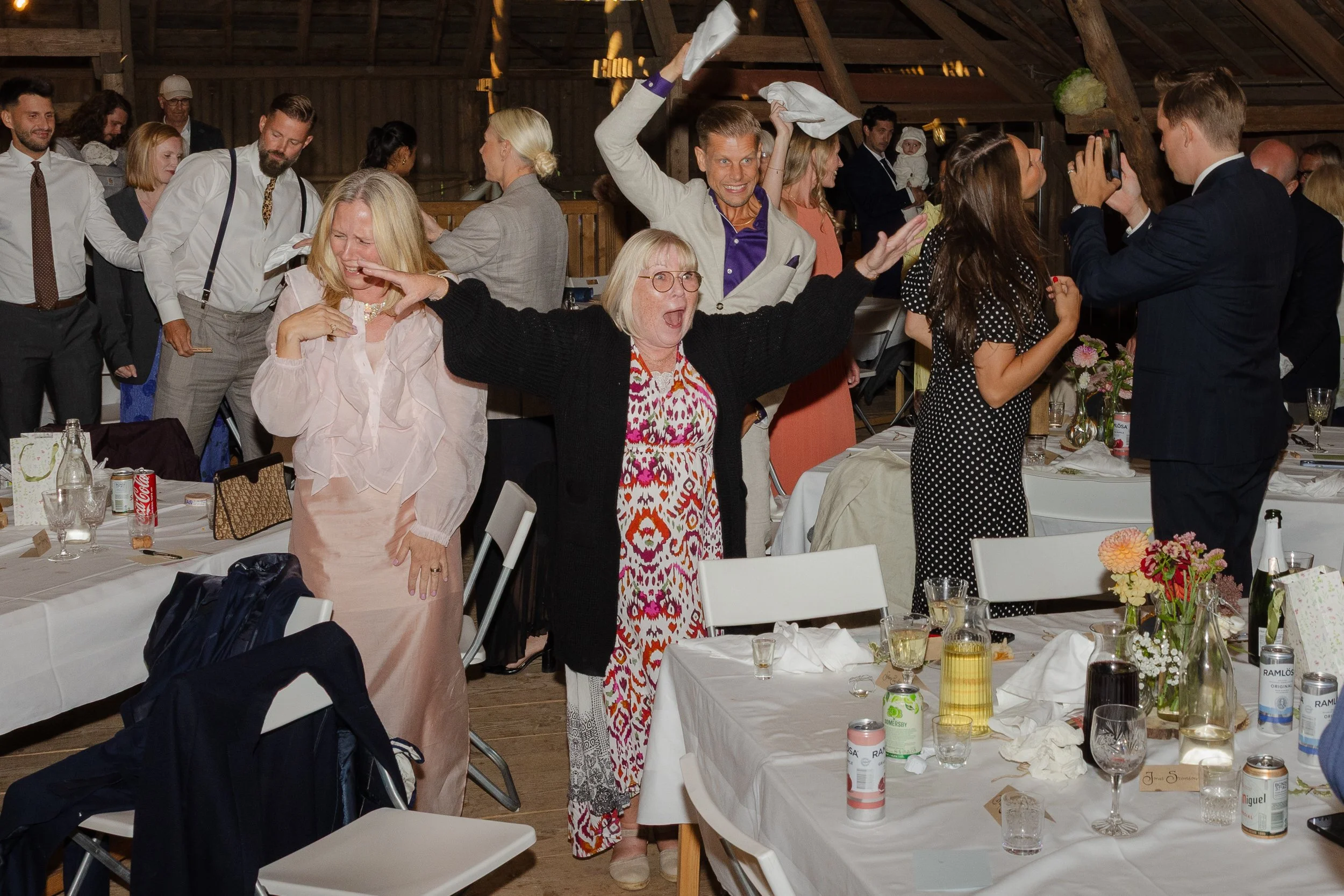 Glada personer på fest i ett rustikt träloft, några dansar och tar bilder, andra pratar och skrattar