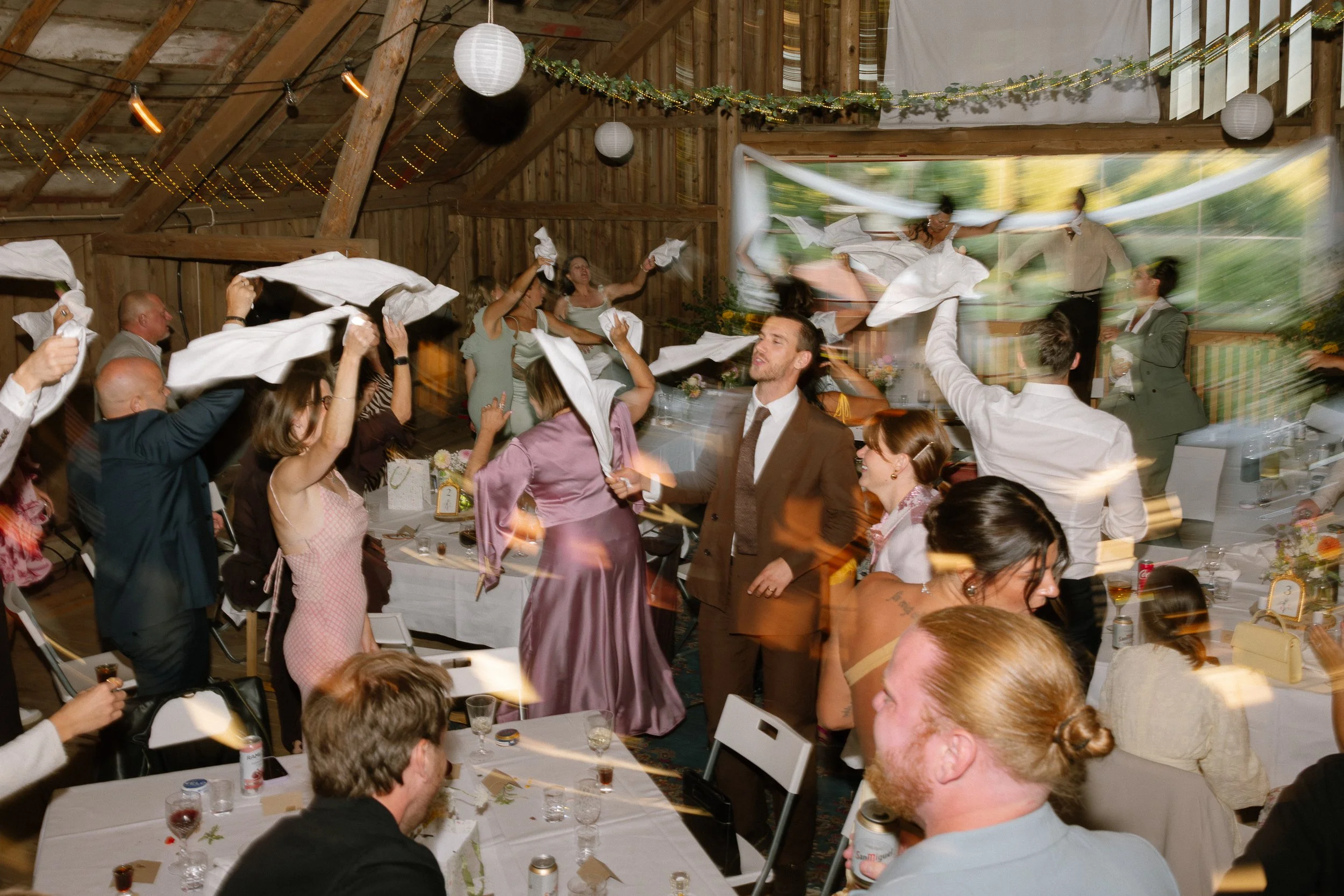Folk dansar och kastar servetter på ett festligt sällskap i en lada  Av Sofia Wilhelmina bröllopsfotograf i Stockholm.