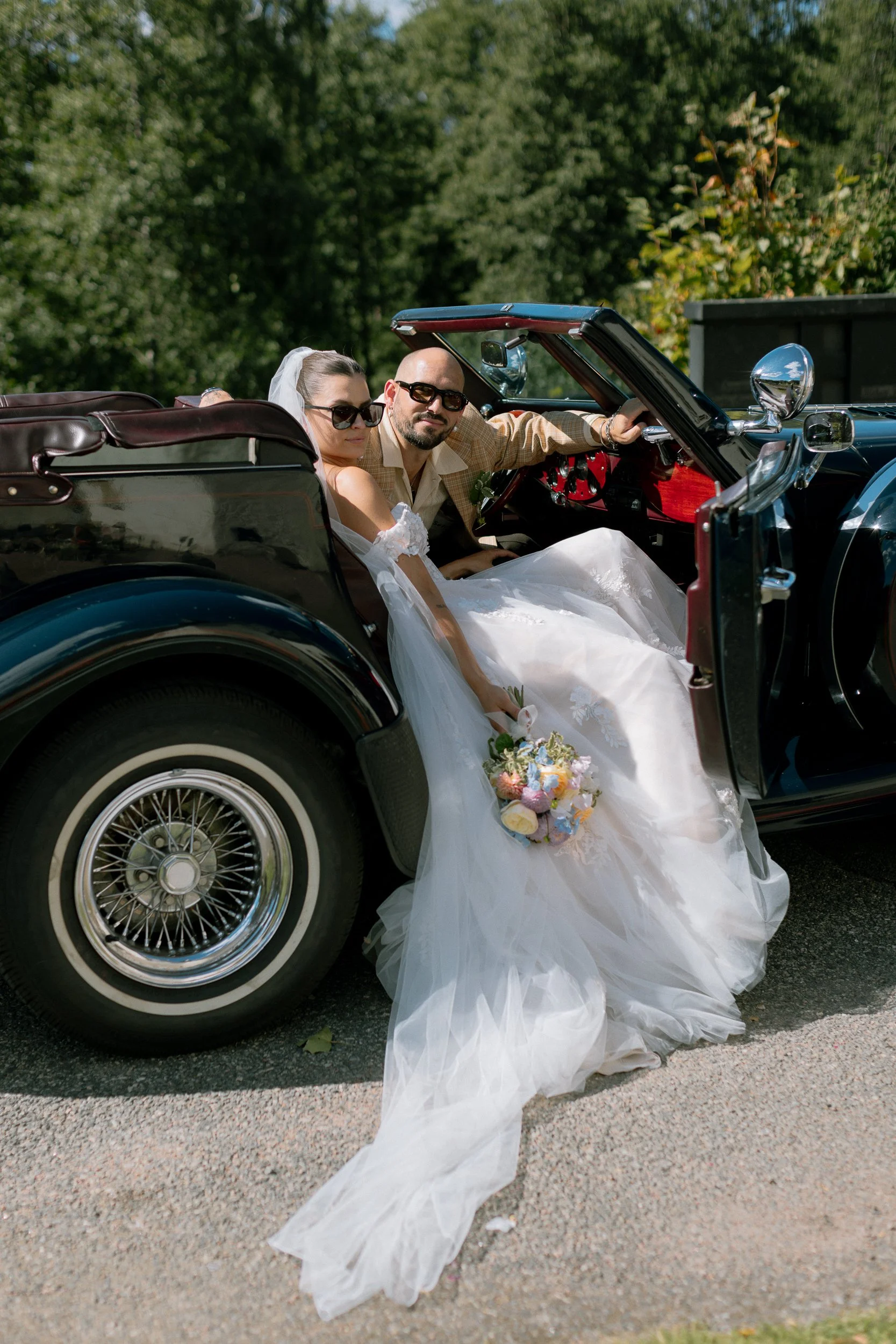 En nygift brud och brudgum i en vintage bil utomhus på sommaren.  Av Sofia Wilhelmina bröllopsfotograf i Stockholm.