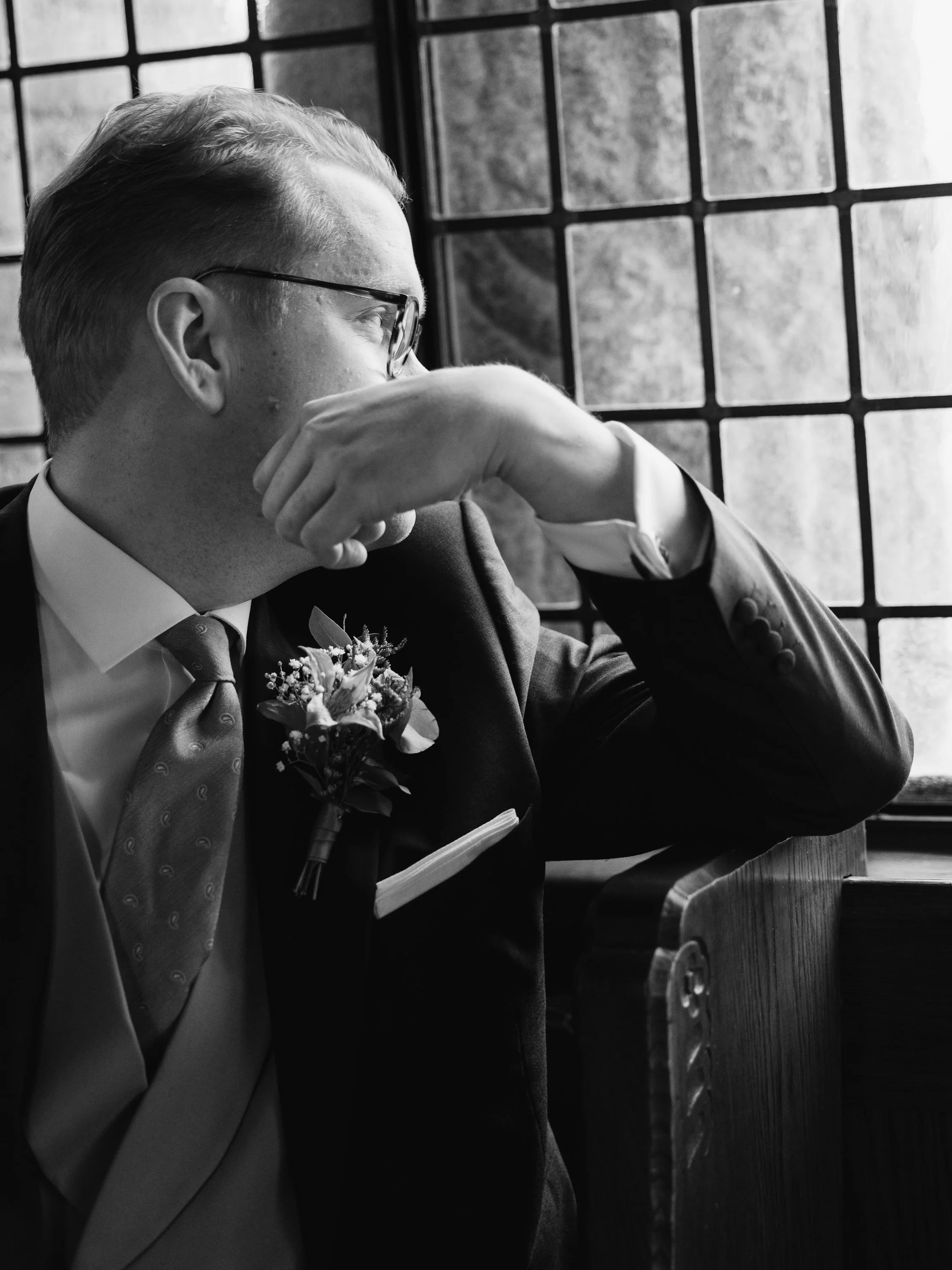 En svartvit bild av en man i kostym som tittar ut genom ett fönster, med händerna vilande mot ansiktet, Engelbrektskyrkan i Stockholm.