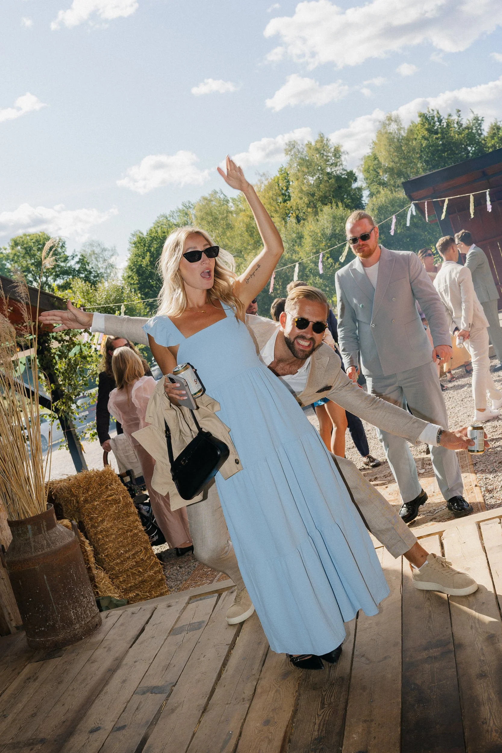 Människor som dansar och har roligt utomhus på en fest dagtid, med gröna träd och ett blått himmel med vita moln.  Av Sofia Wilhelmina bröllopsfotograf i Stockholm.