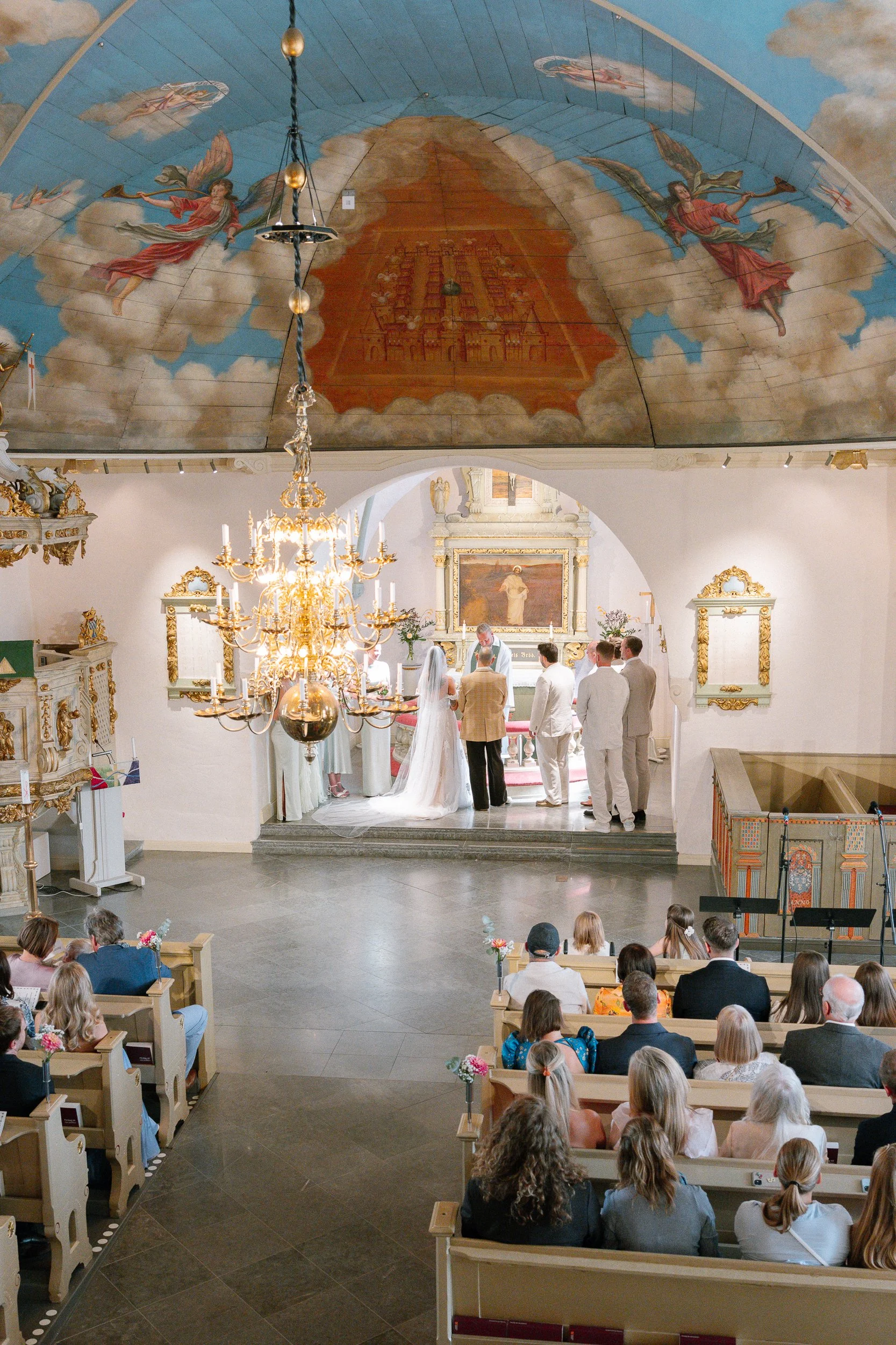 En brud och brudgummi församlingar i en kyrka under deras bröllopsceremoni, med gäster som tittar.
